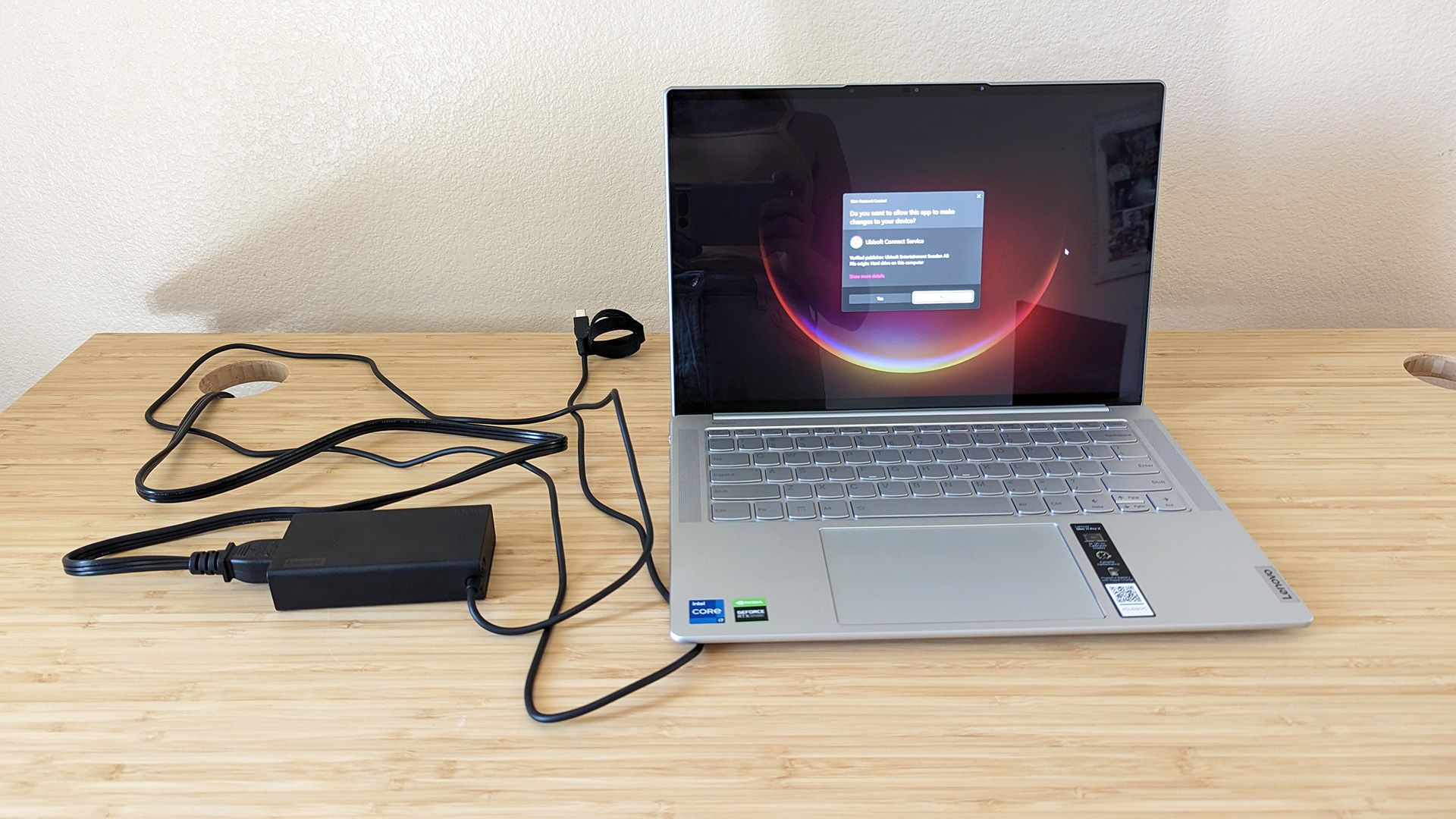 The Lenovo Slim 7i Pro X laptop on a desk with the AC adapter.