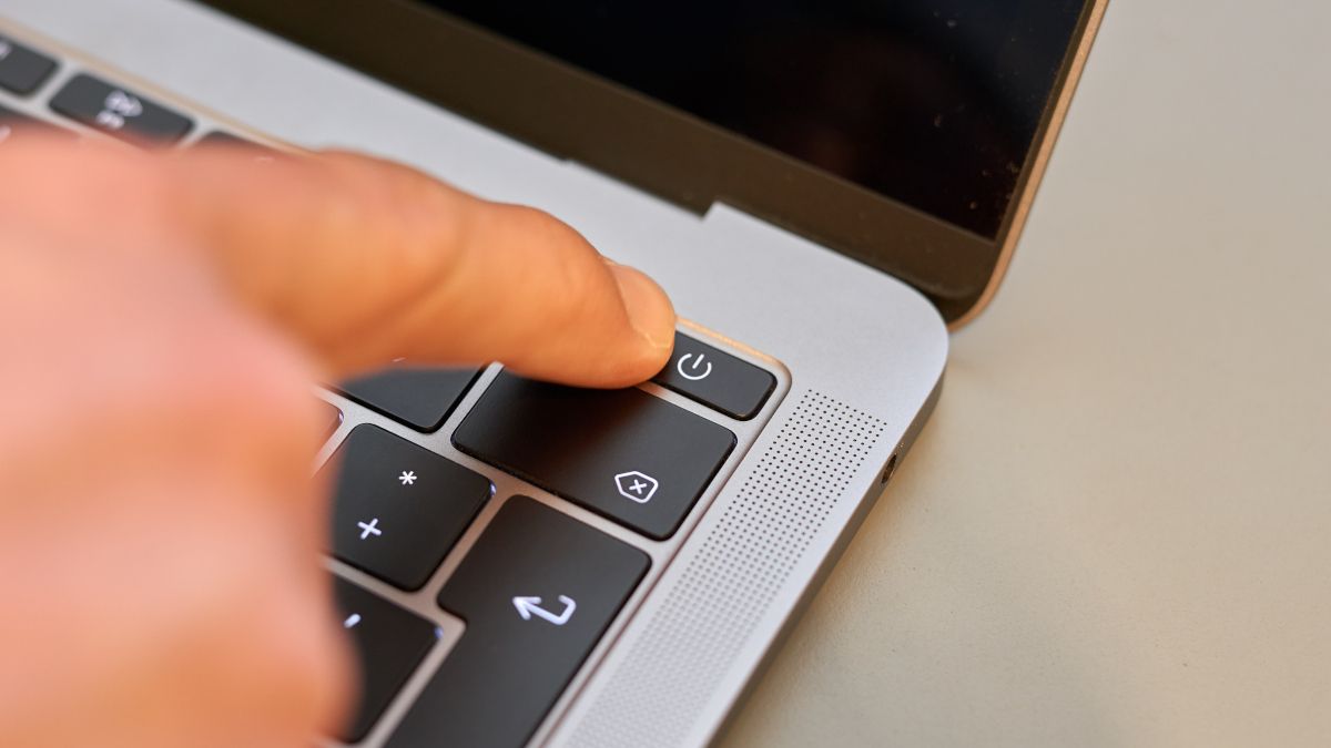 Person's finger pressing the power button on a notebook computer.