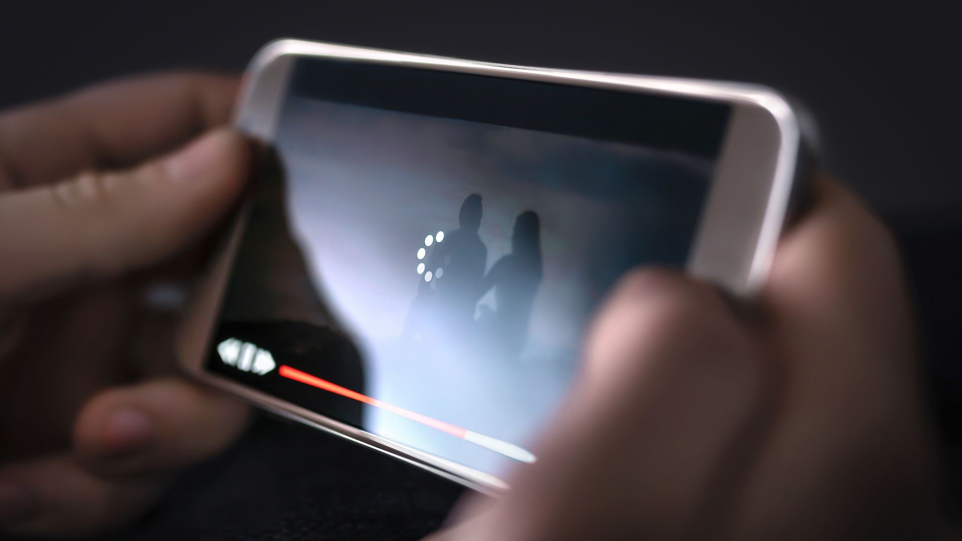 A man holding a mobile device with a loading icon on a playing video.
