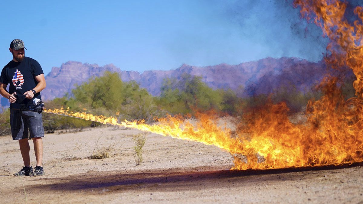 A man using a flame thrower out in the desert.
