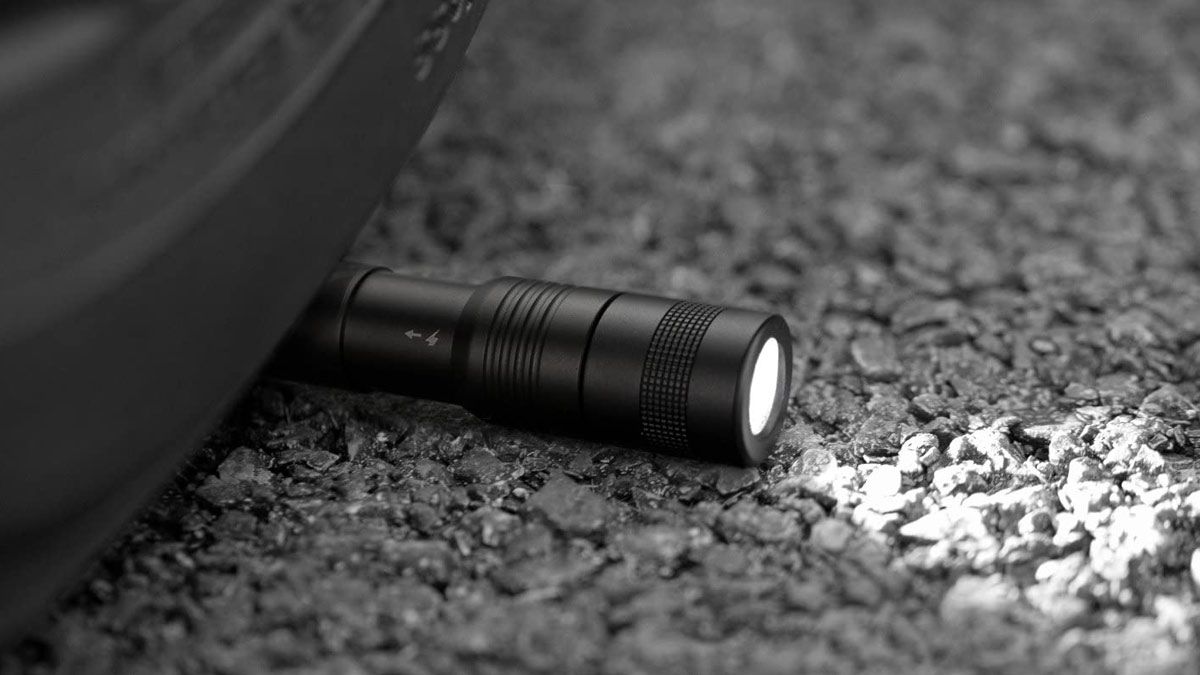 A rugged Anker pen light flashlight laying on the road under a tire.