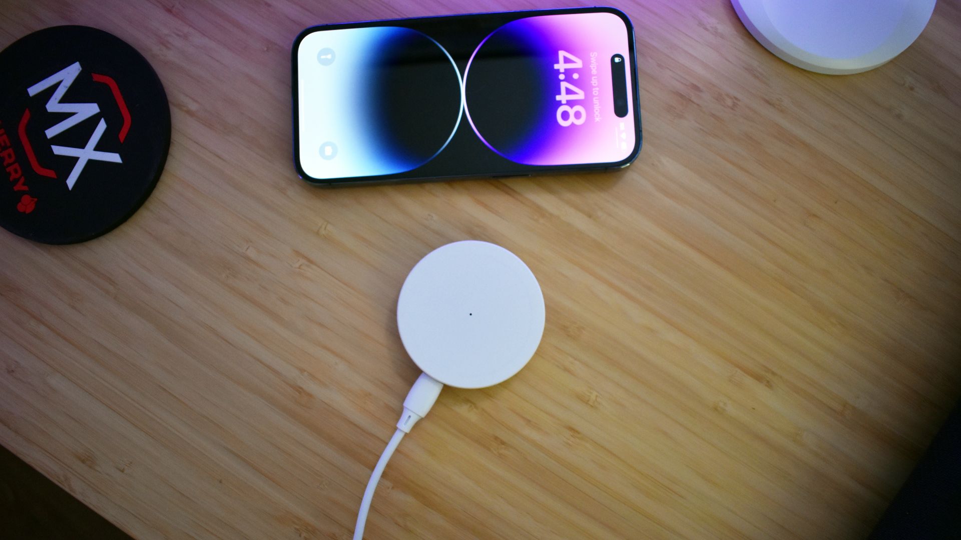 HaloLock Shift Wireless Charger puck on desk next to iPhone 14 Pro and drink coaster