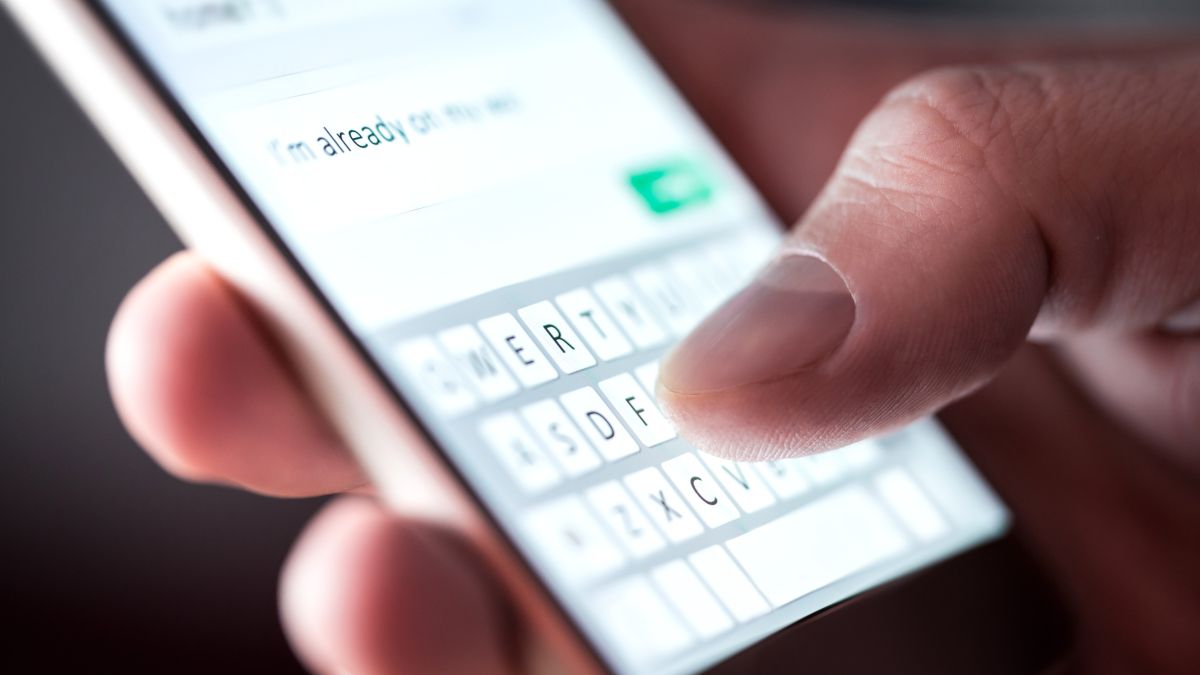 Closeup of a person's fingers typing on a message smartphone keyboard.