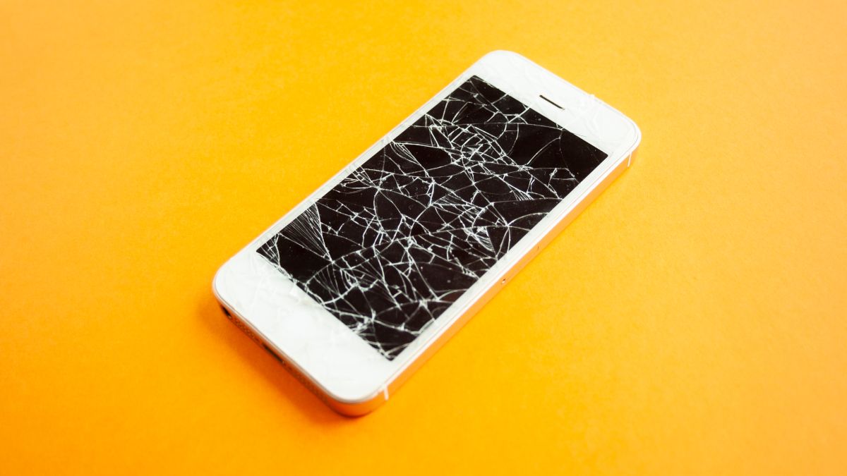 A white smartphone with a severely cracked screen on a yellow background.