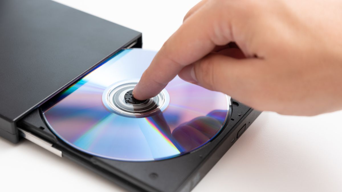 Person's hand putting a CD into a disc drive.