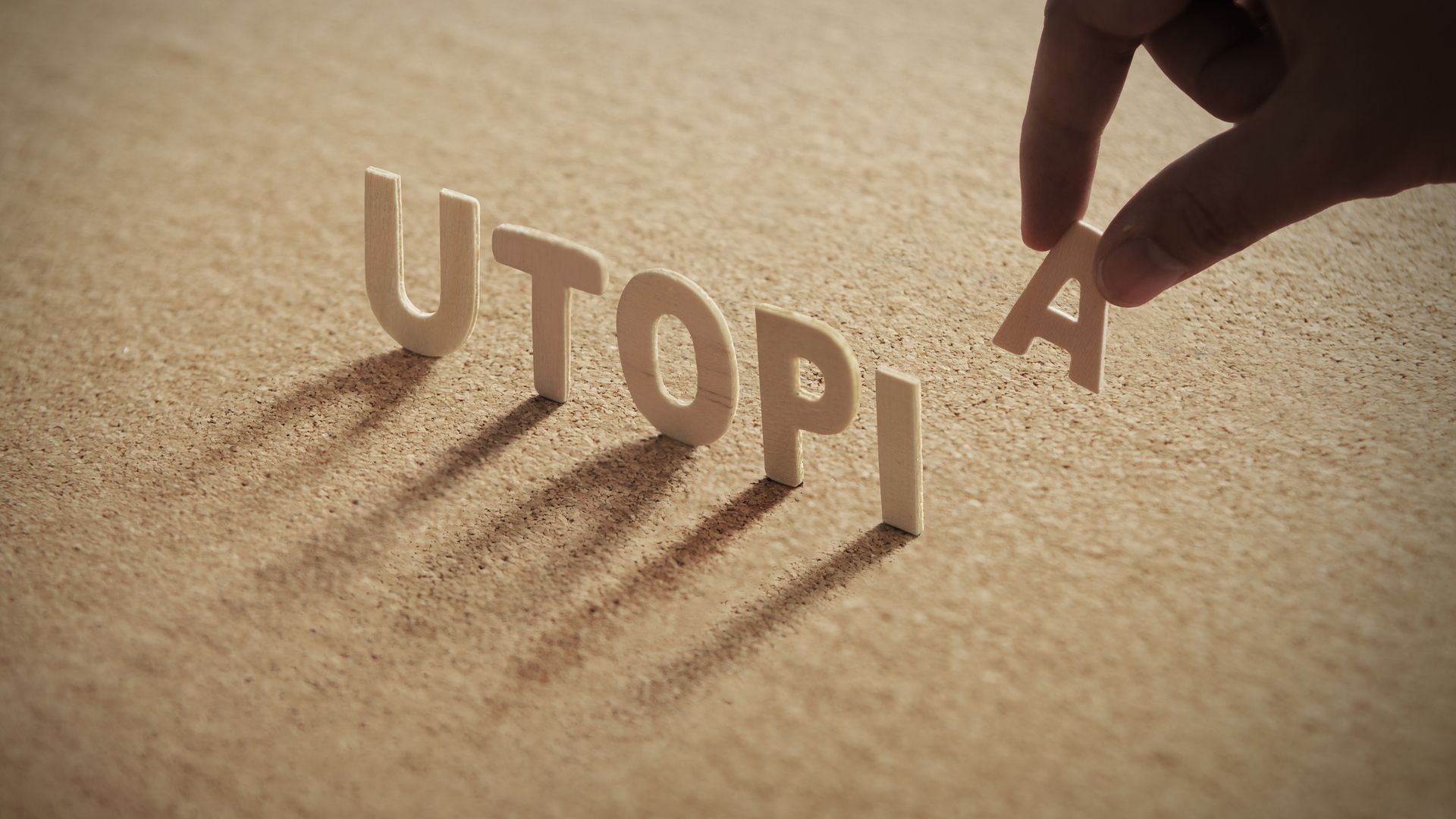 The word &quot;UTOPIA&quot; on a corkboard with human's hand removing the &quot;A&quot;
