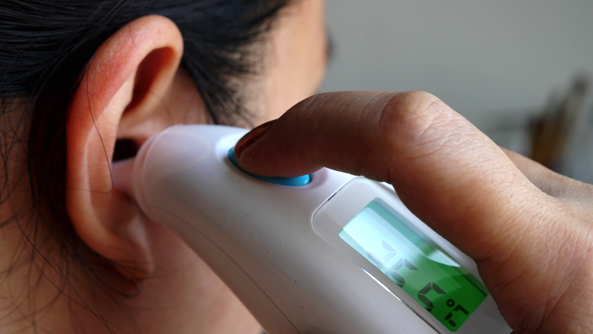 An adult using an ear thermometer on themselves.