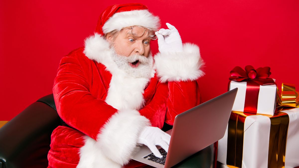 Santa Claus lifting his glasses with a surprised expression and looking at a laptop.
