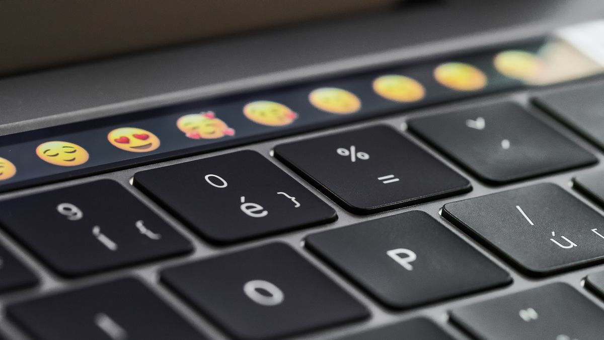 Closeup of a MacBook Pro keyboard with the Touch Bar featuring emoji in focus.