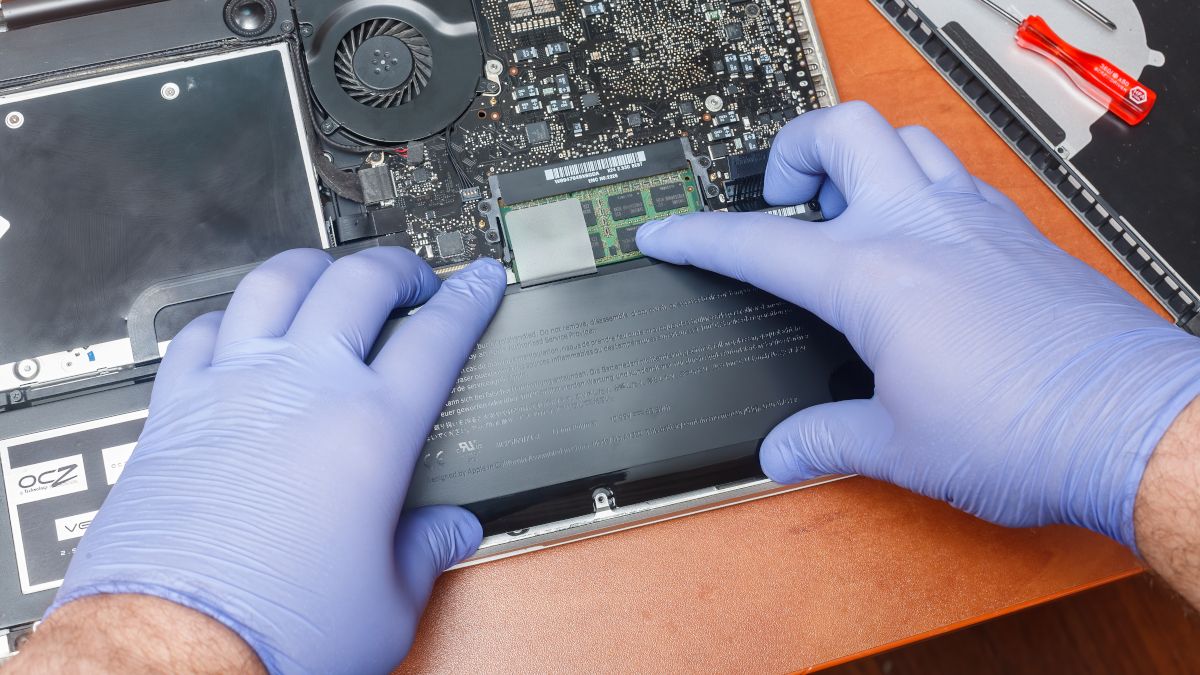 Closeup of a person's gloved hands installing a new battery inside an Apple MacBook.