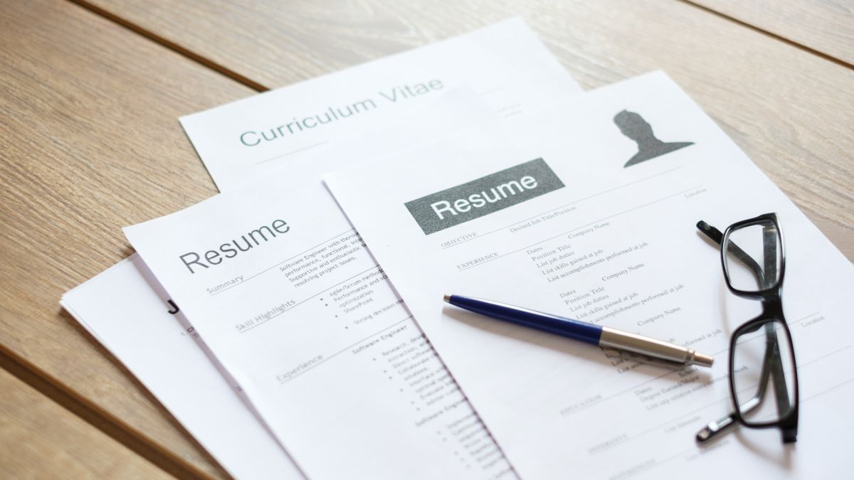 A stack of resumes on a tabletop with a pen and glasses.