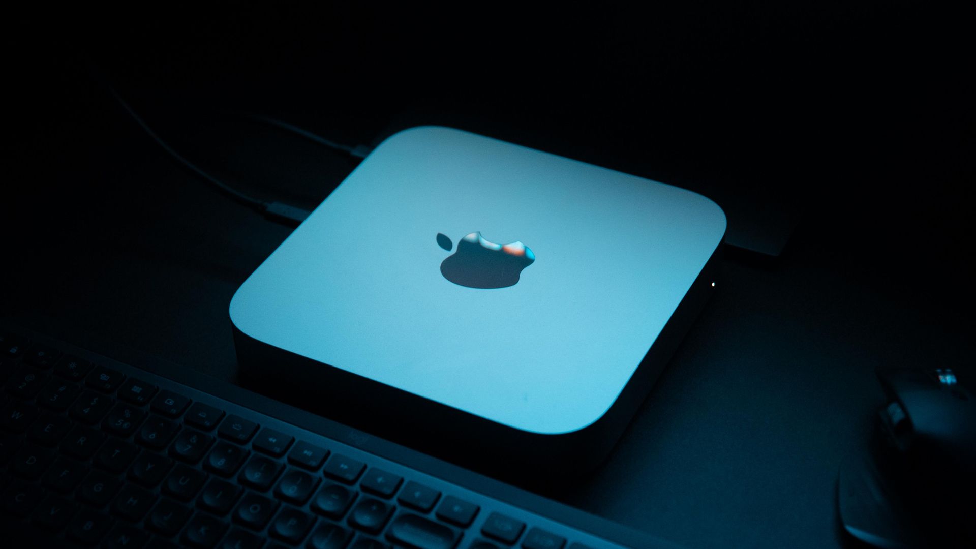A Mac mini on a desk in a dark room under blue mood lighting.