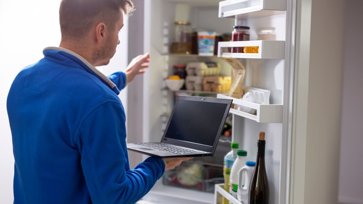 Person holding a laptop in front of an open refrigerator.