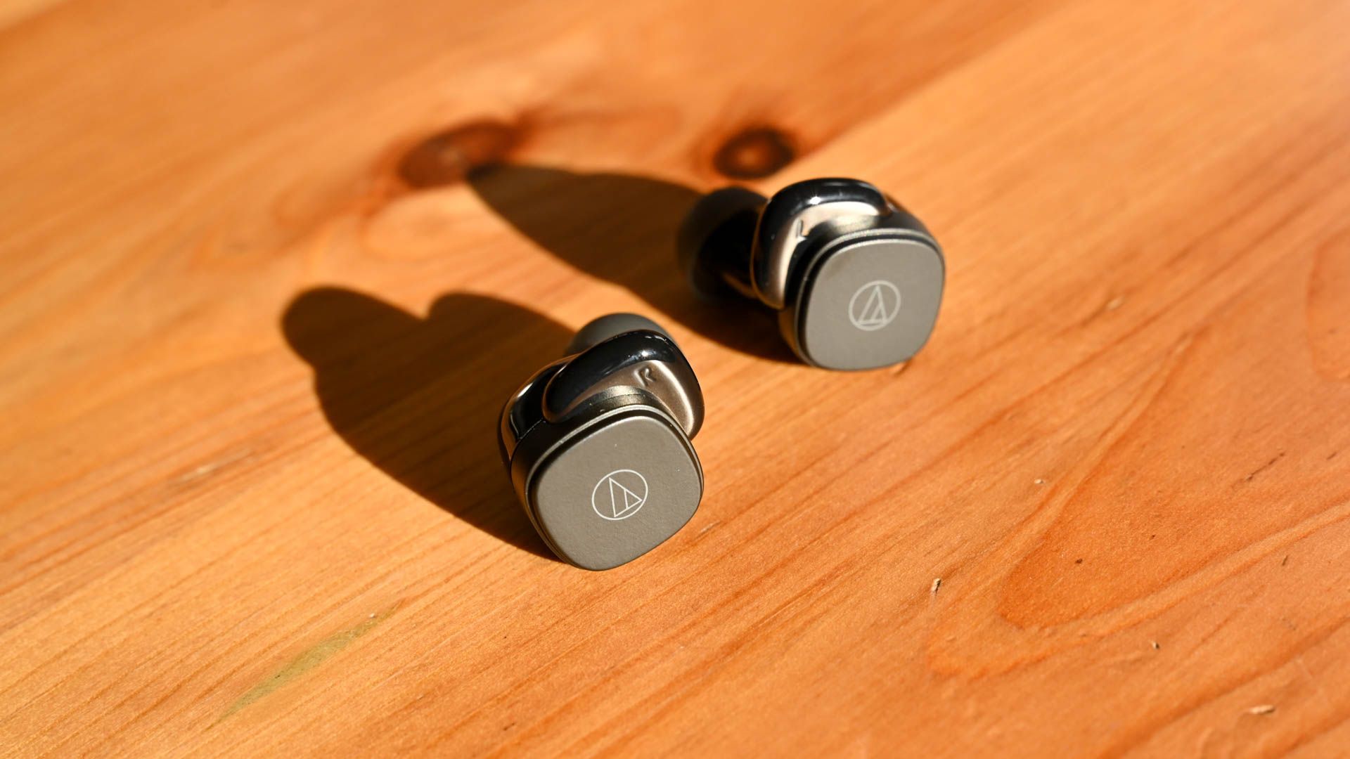 Two Audio Technica ATH-SQ1TW earbuds on a wood table