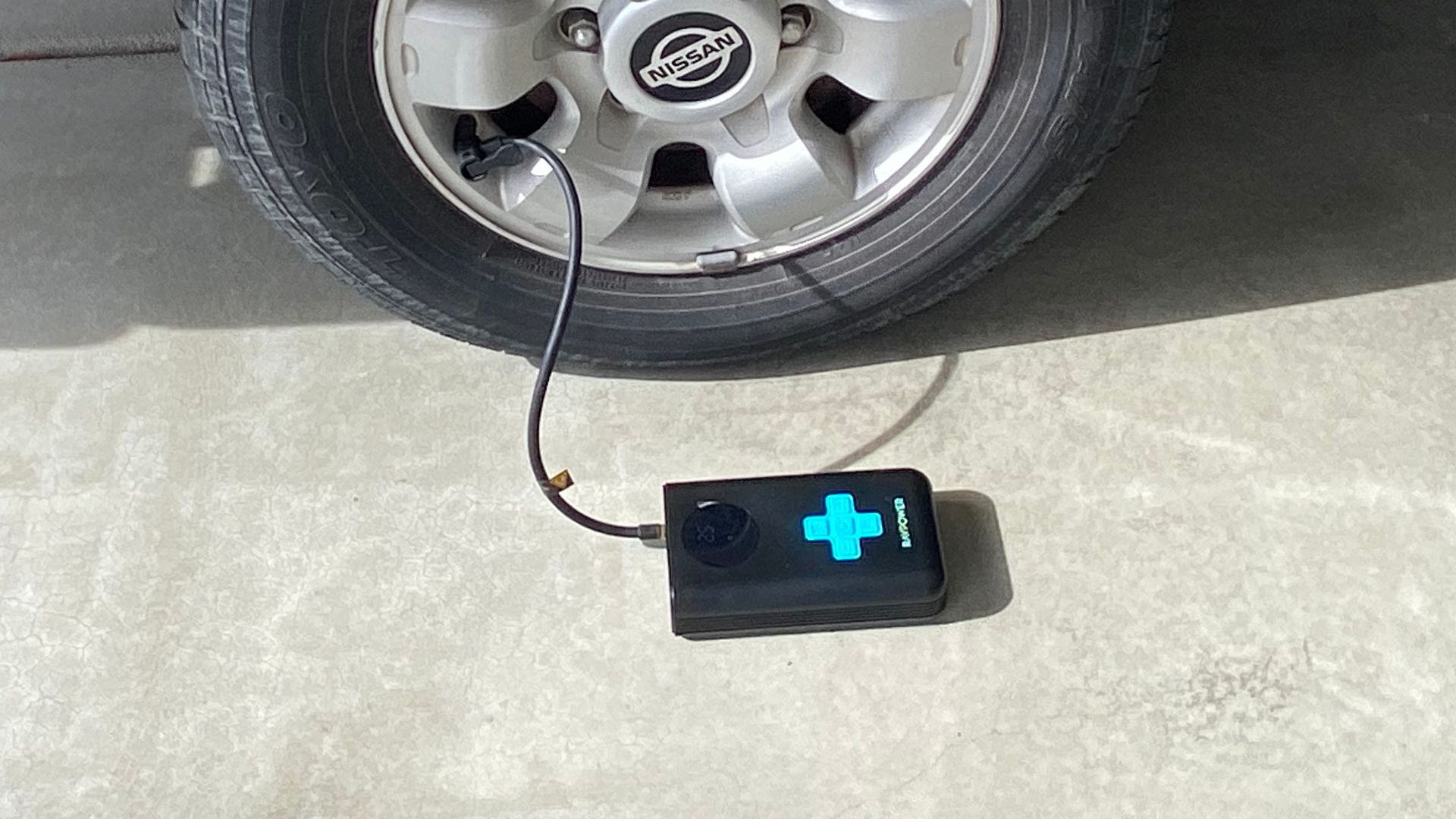 The RAVPower Jump Starter With Air Compressor attached to a tire.