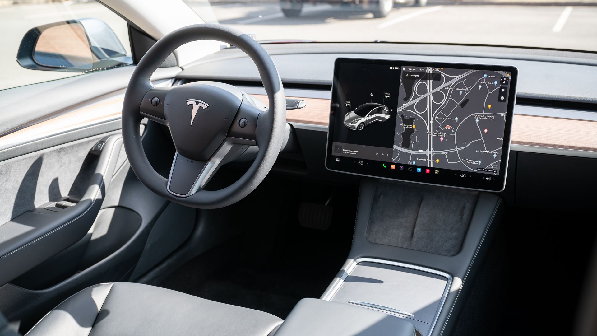 Door handle, steering wheel, infotainment display, wireless chargers, and storage inside the Tesla Model 3