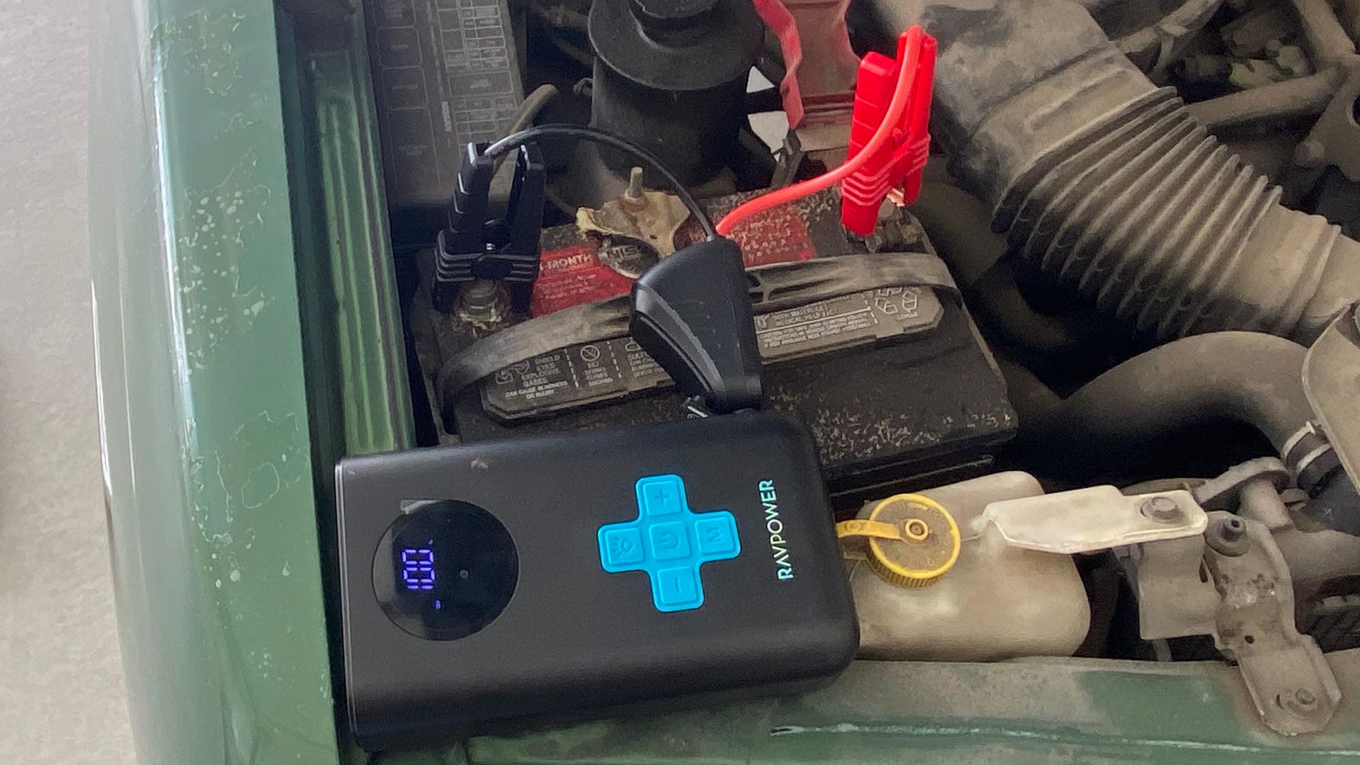 The RAVPower Jump Starter With Air Compressor hooked up to an old truck battery.