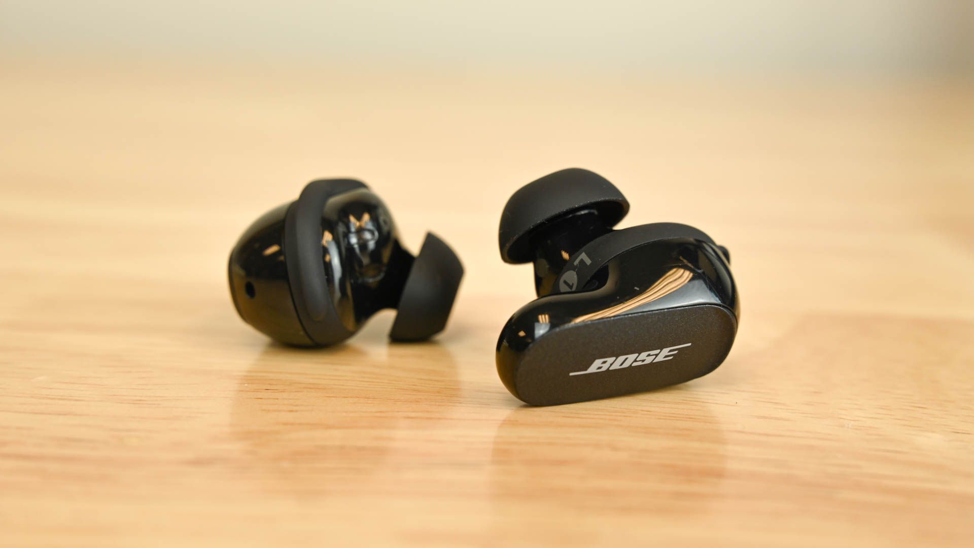 A pair of Bose QuietComfort Earbuds 2 sitting on a wood table
