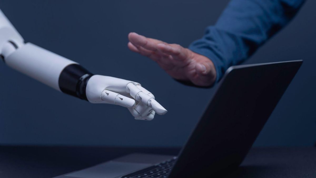 Man blocking robot hand above laptop