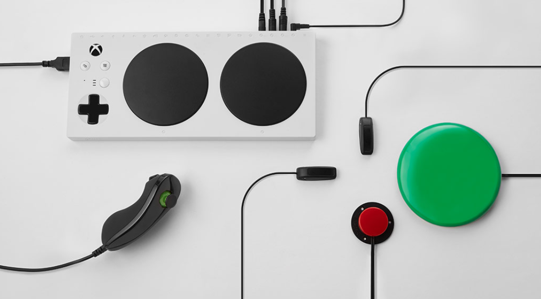 An Xbox Adaptive Controller connected to a joystick, a small red button, and a large green button through some of its 3.5mm ports.