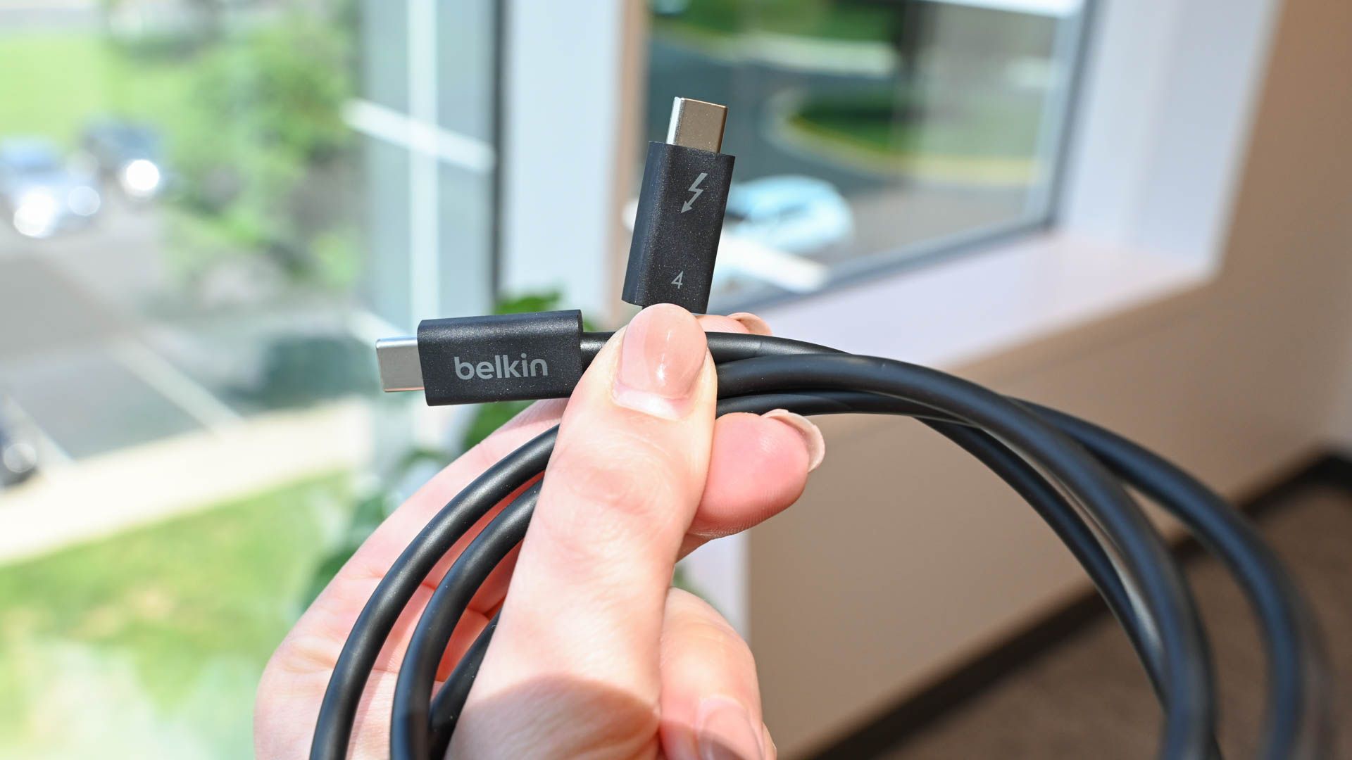 Person holding a Belkin Thunderbolt 4 cable near a window