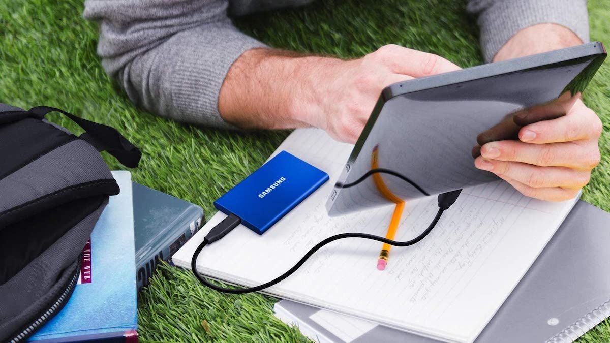 Blue SSD plugged into a tablet held by a man in the grass.