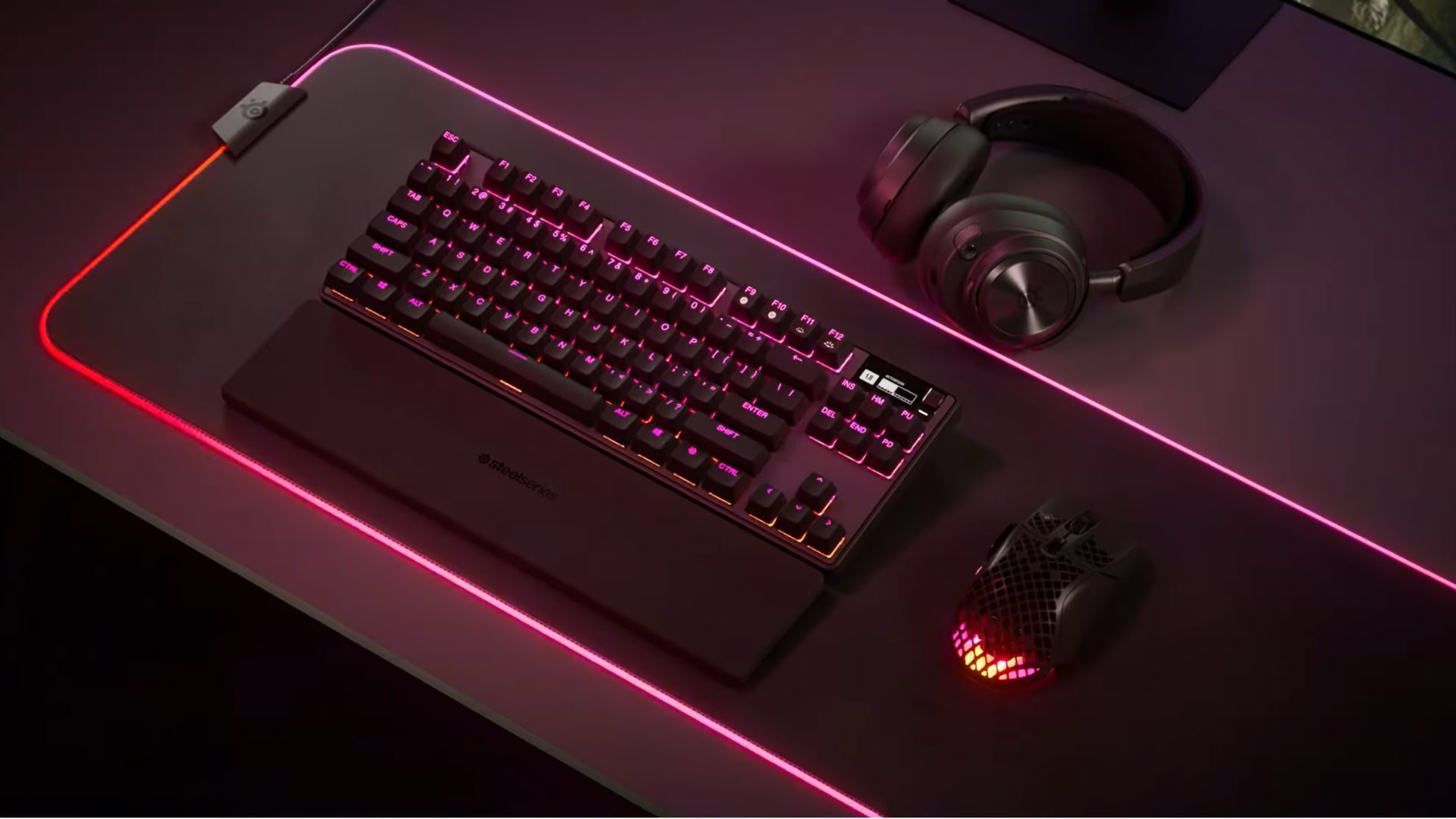 SteelSeries Apex Pro TKL sur une table de jeu avec des lumières rouges et roses.