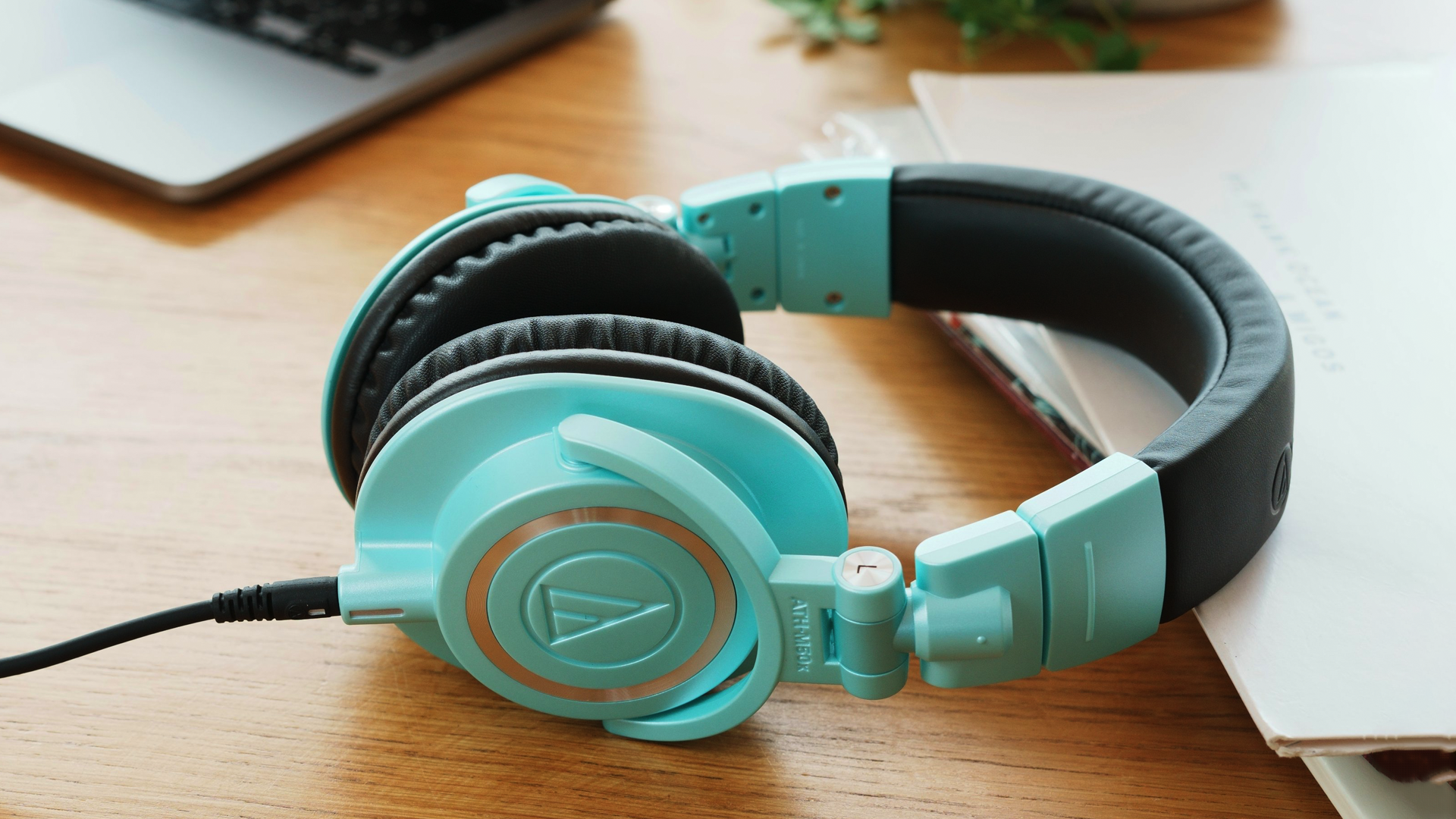 The Audio-Technica ATH-M50x Ice Blue headphones lying on a wooden table.