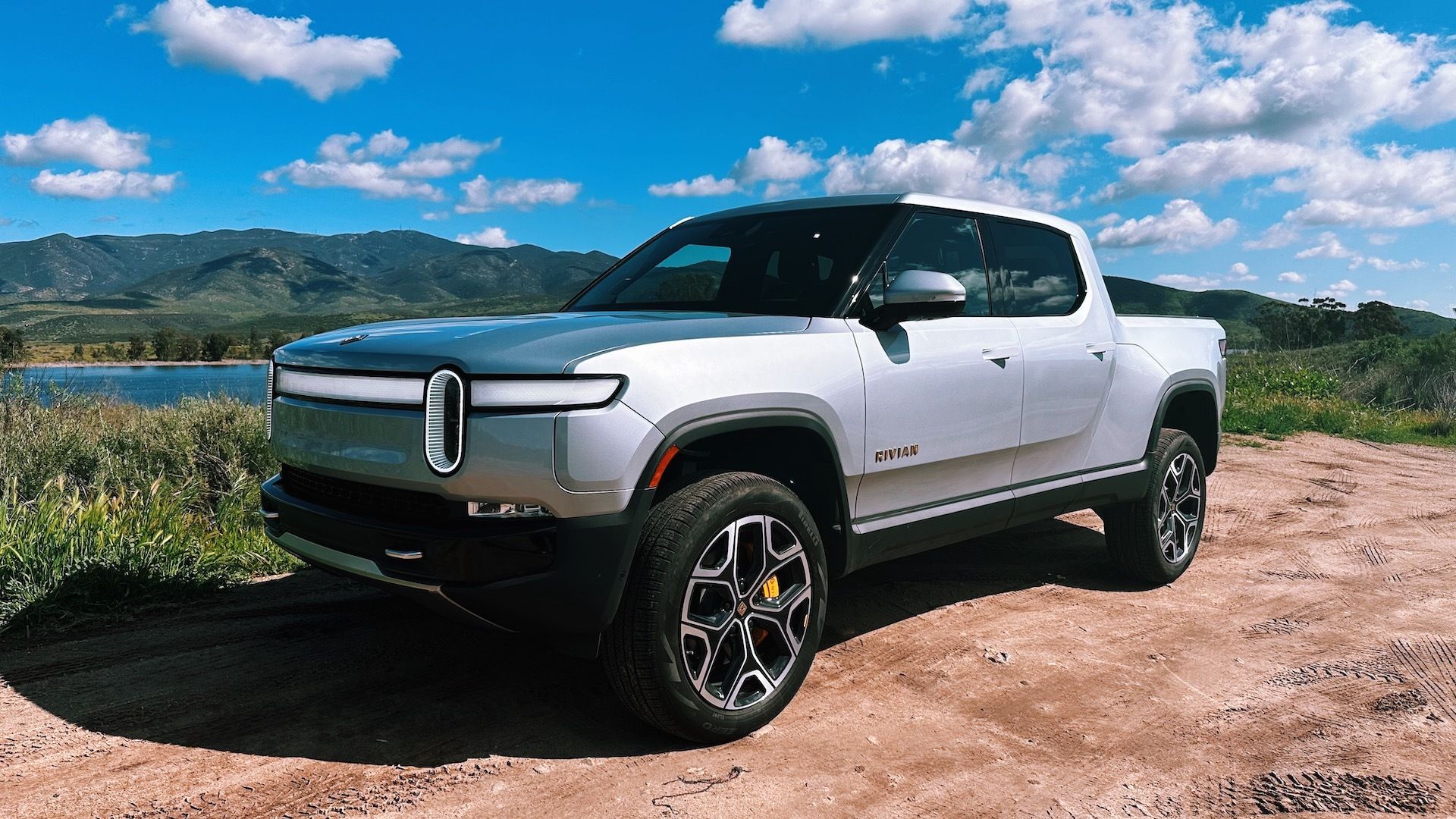 Rivian's R1T electric truck is parked off-road by a lake in the mountains. 