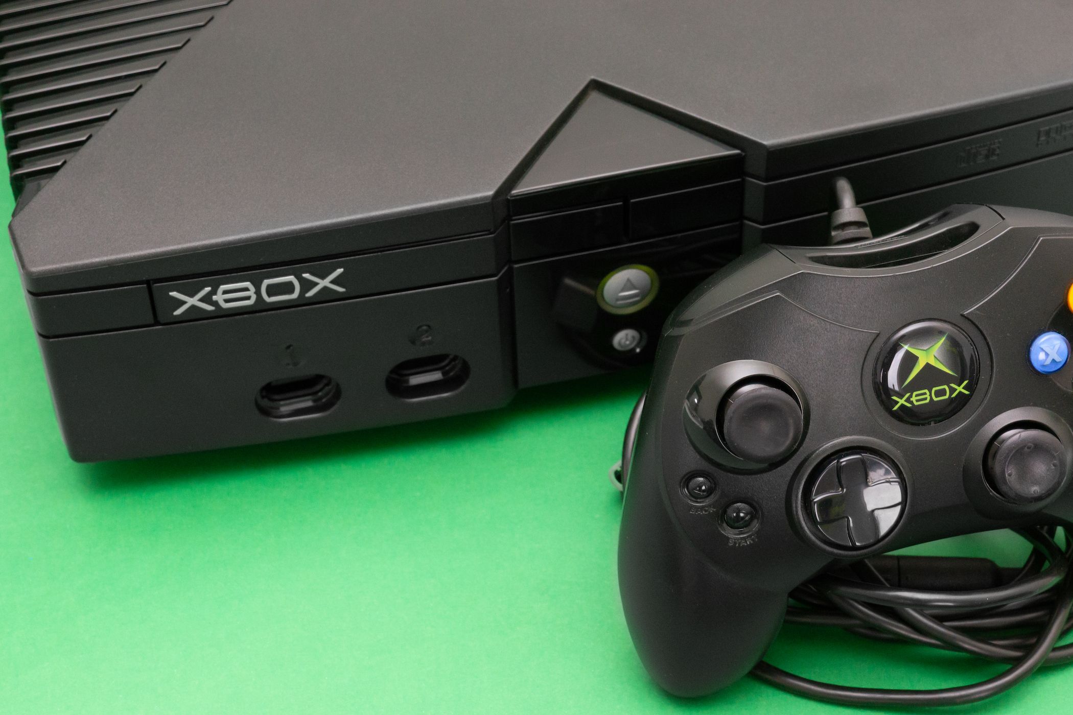 Microsoft’s original Xbox console powered on, on a green surface, and with a Controller S sitting in-front.