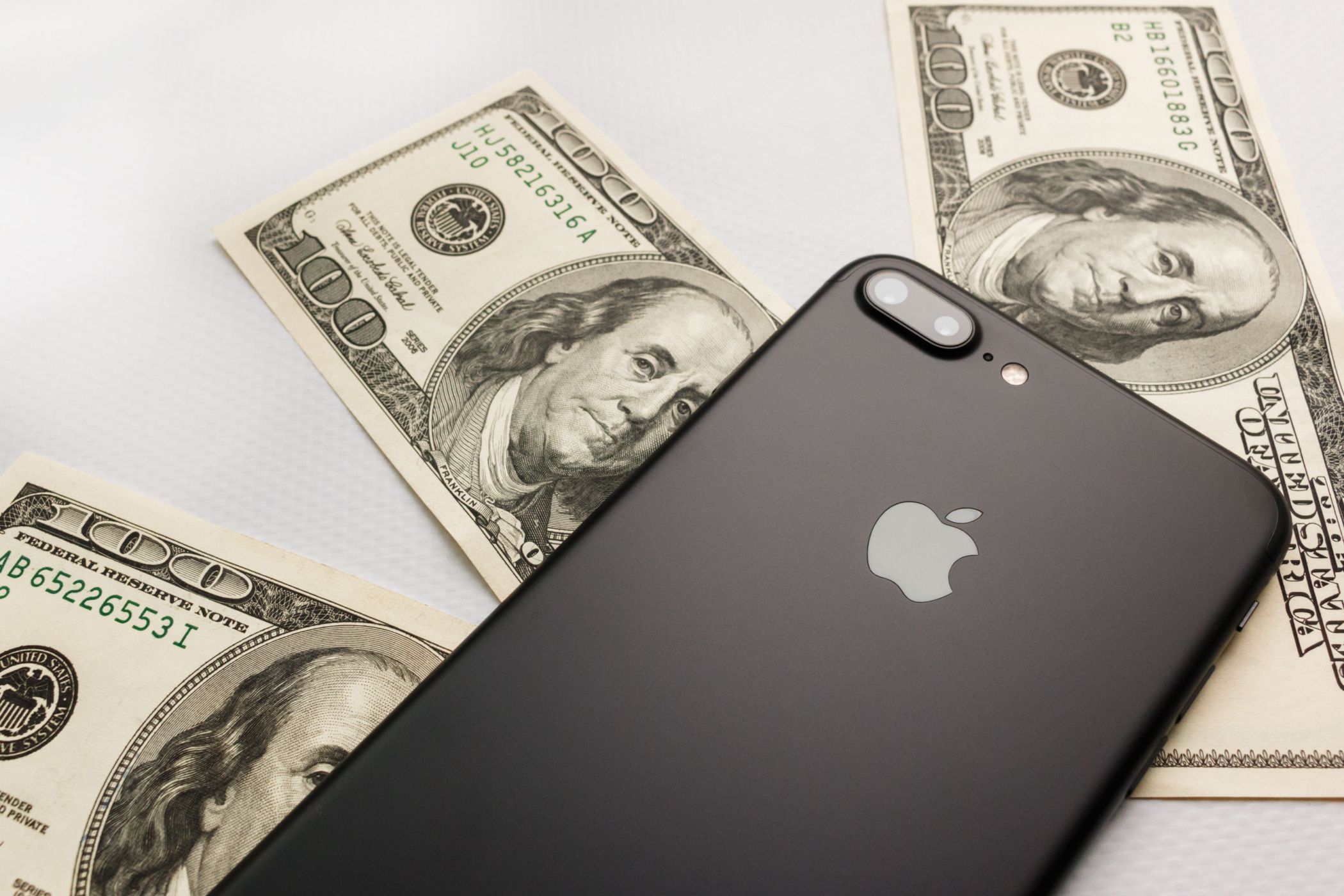 Black iPhone 8s plus on three hundred dollar bills.