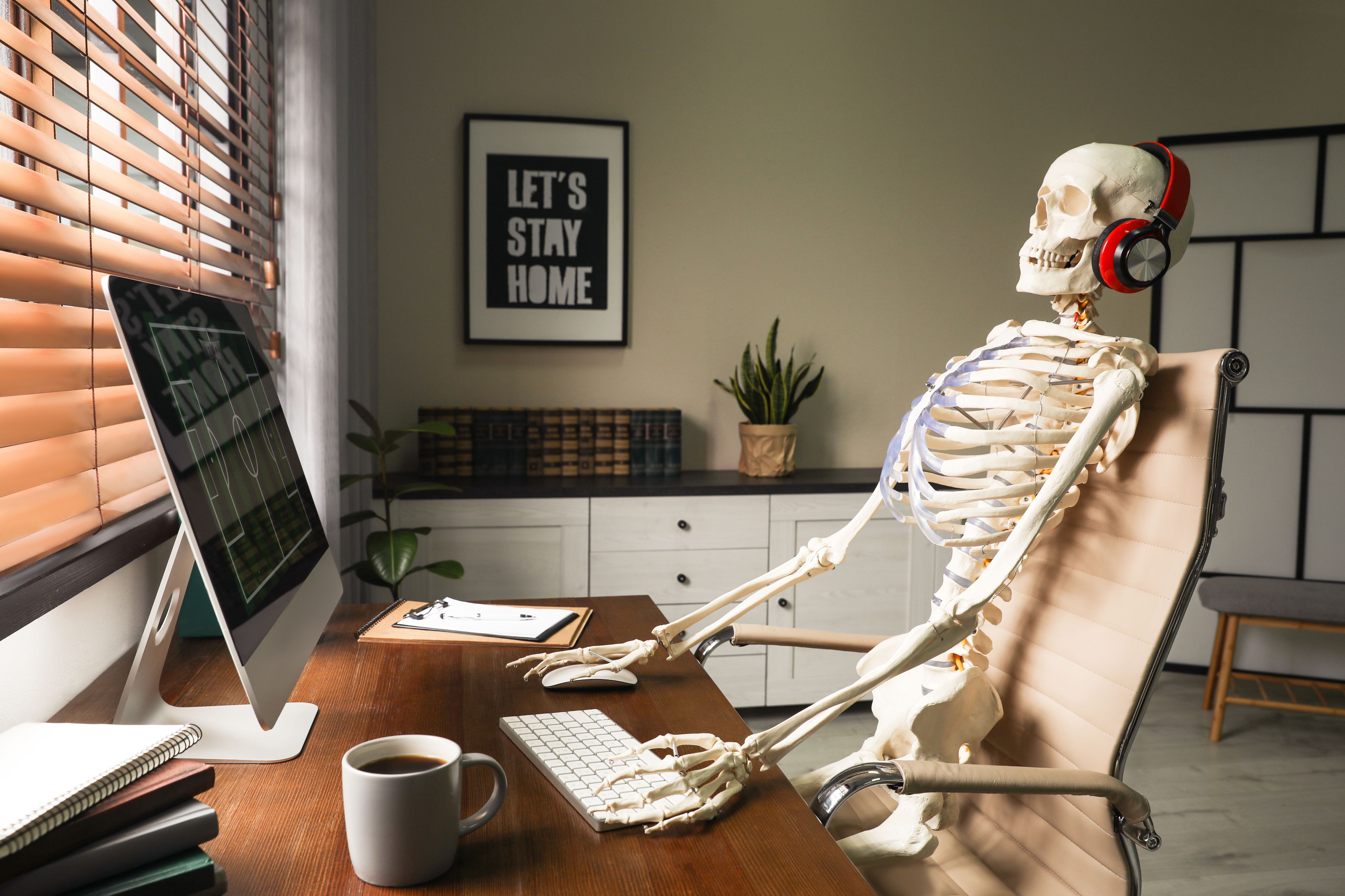 Human skeleton sat at a computer desk with headphones on.