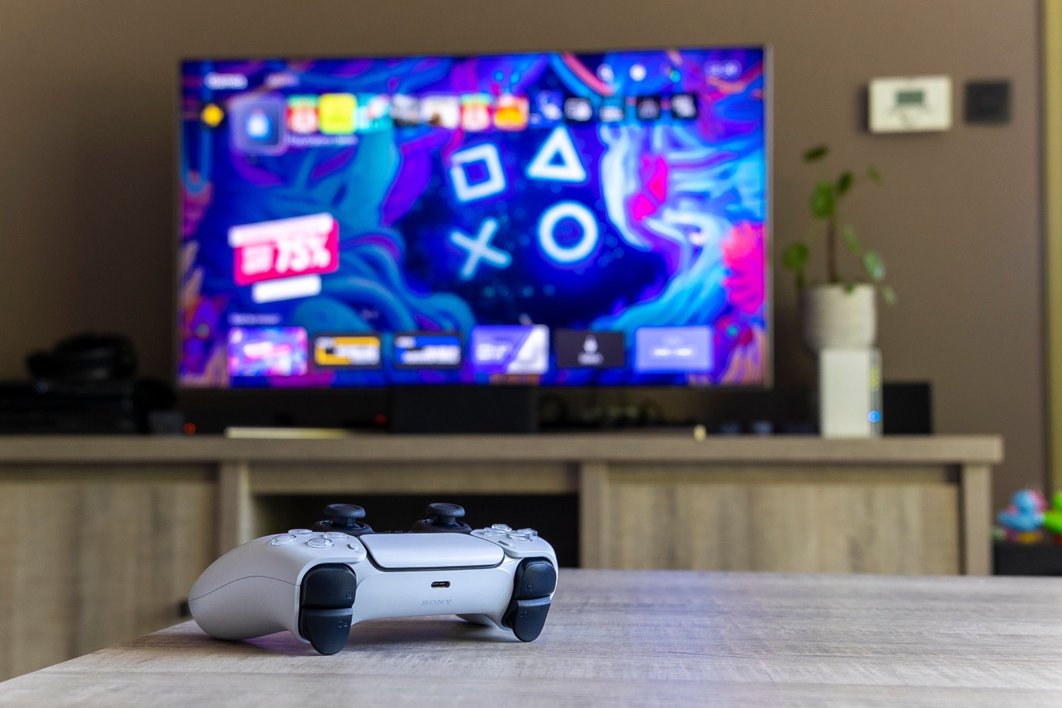 PlayStation 5 DualSense controller sitting on a coffee table in front of a TV.