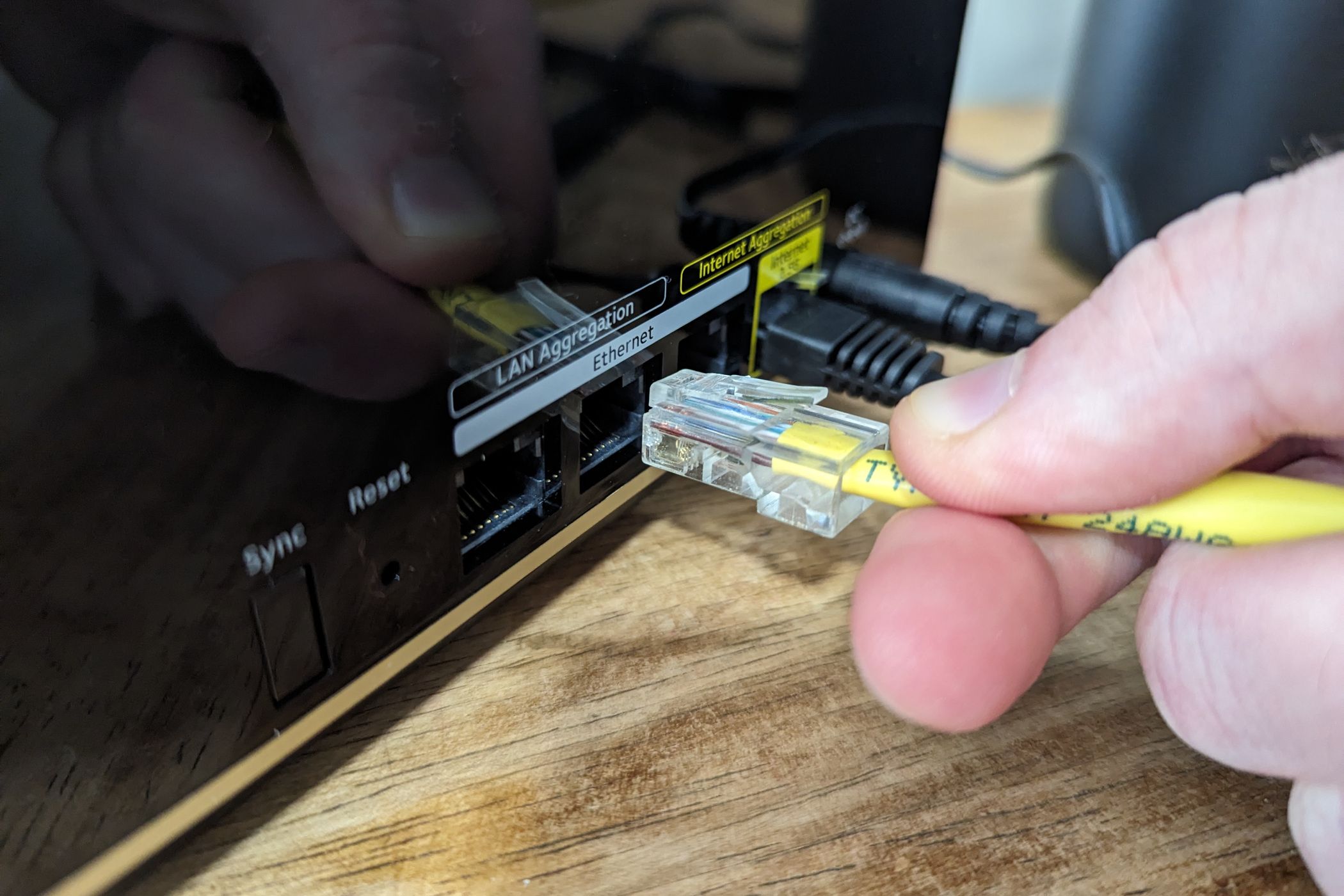 Person plugging an Ethernet cable into a port on the Netgear Nighthawk MK93S Tri-Band Mesh Wifi 6E System.