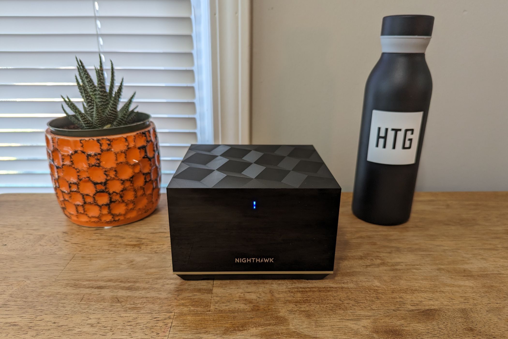 A Netgear Nighthawk Tri-Band Mesh Wifi 6E router on a wood table next to a water bottle reading 