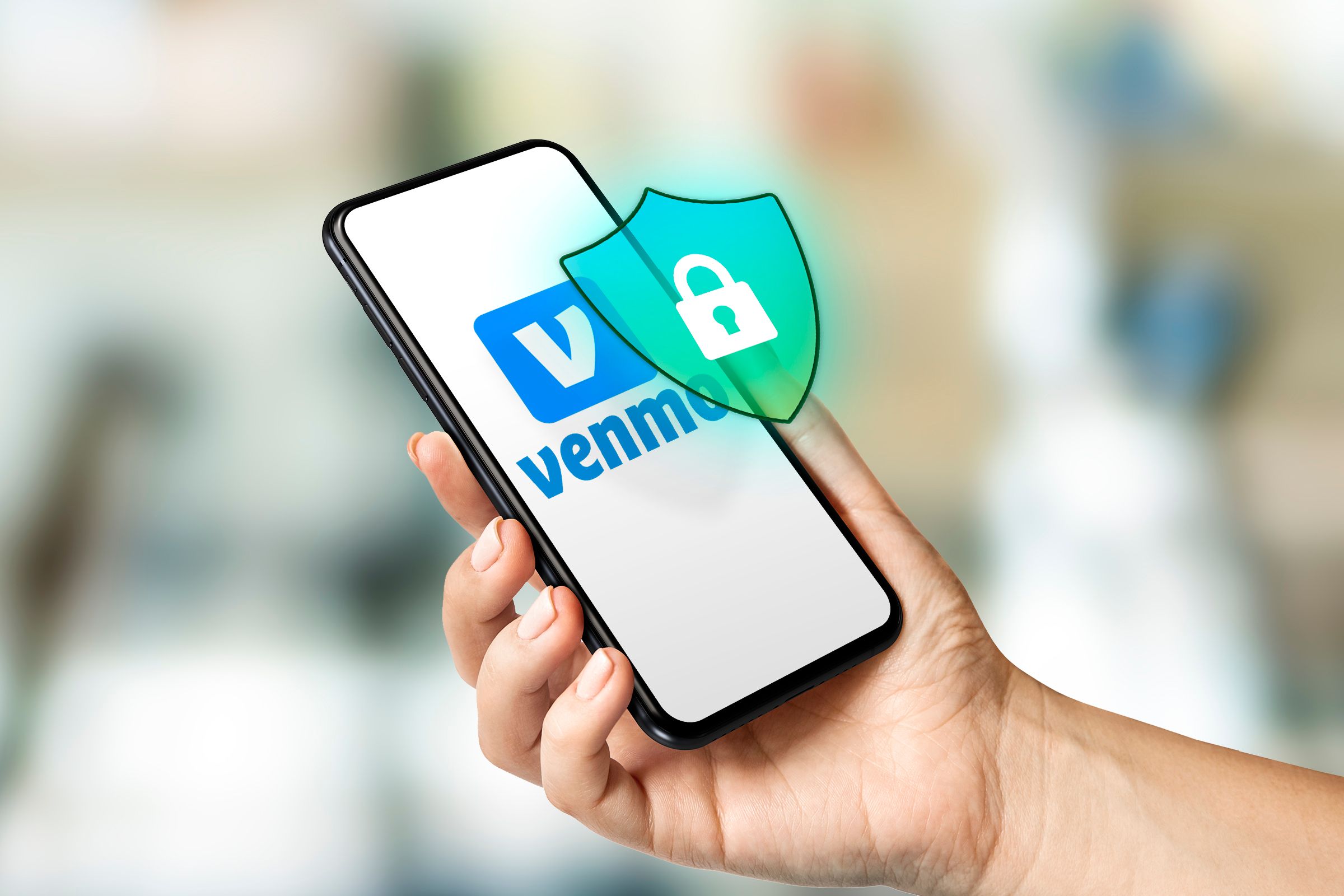 A hand holding a smartphone with Venmo logo on the screen and a security shield above the screen