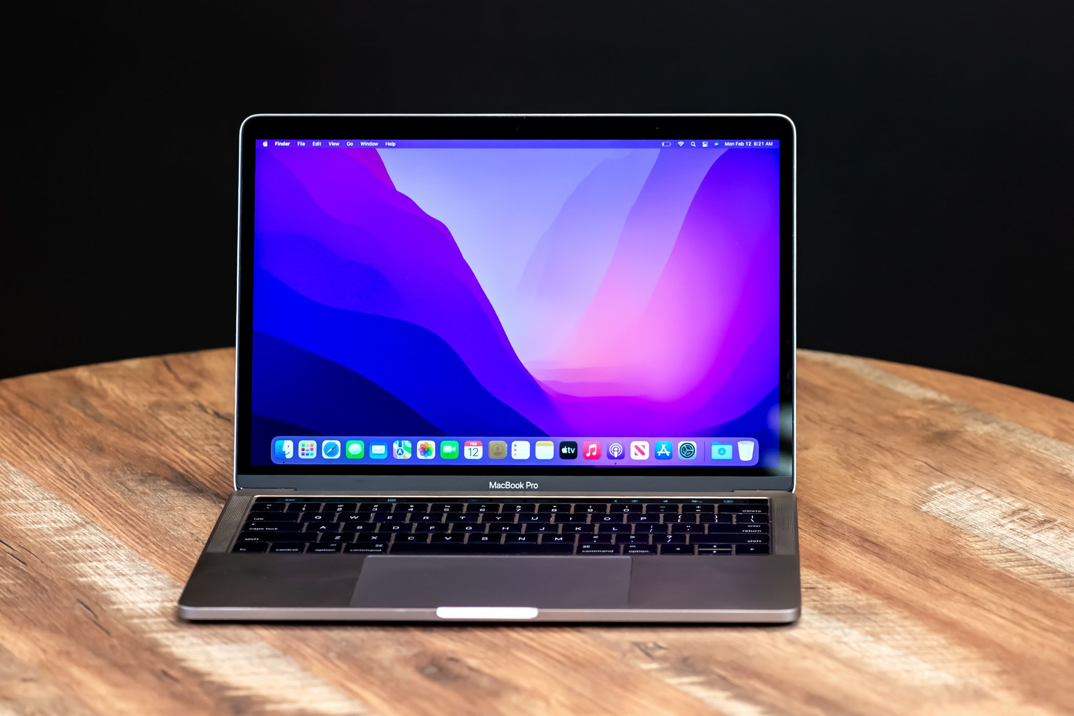 MacBook on a desk showing a colorful wallpaper with in a dark room.