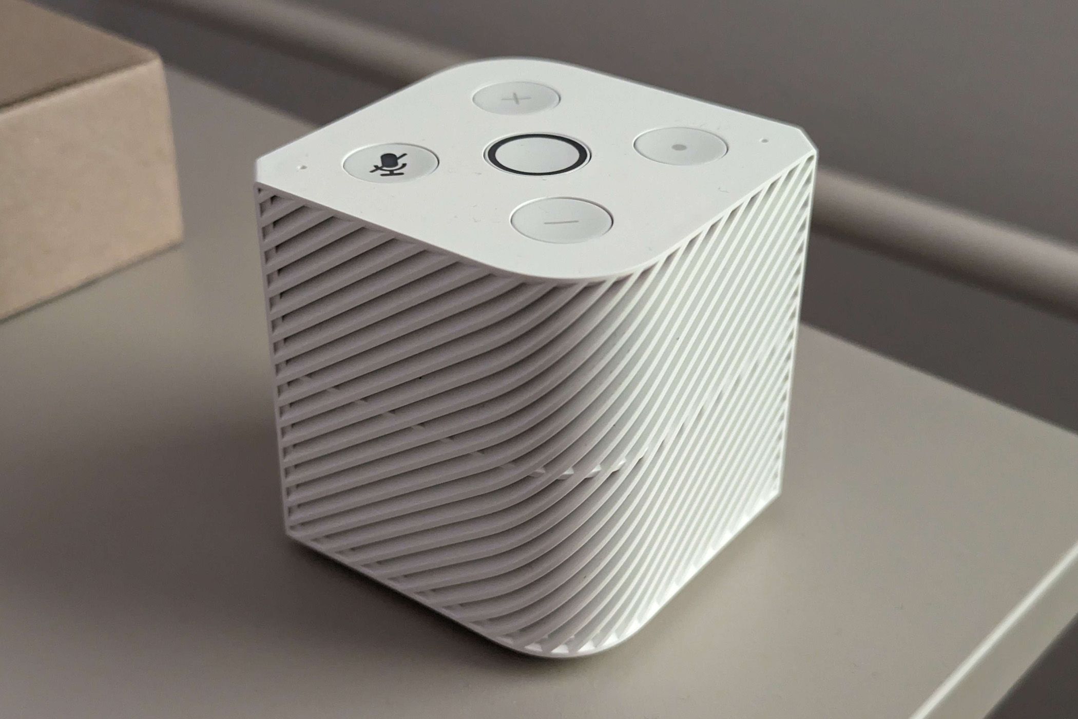 White cubic smart speaker with buttons on top, placed on a table.