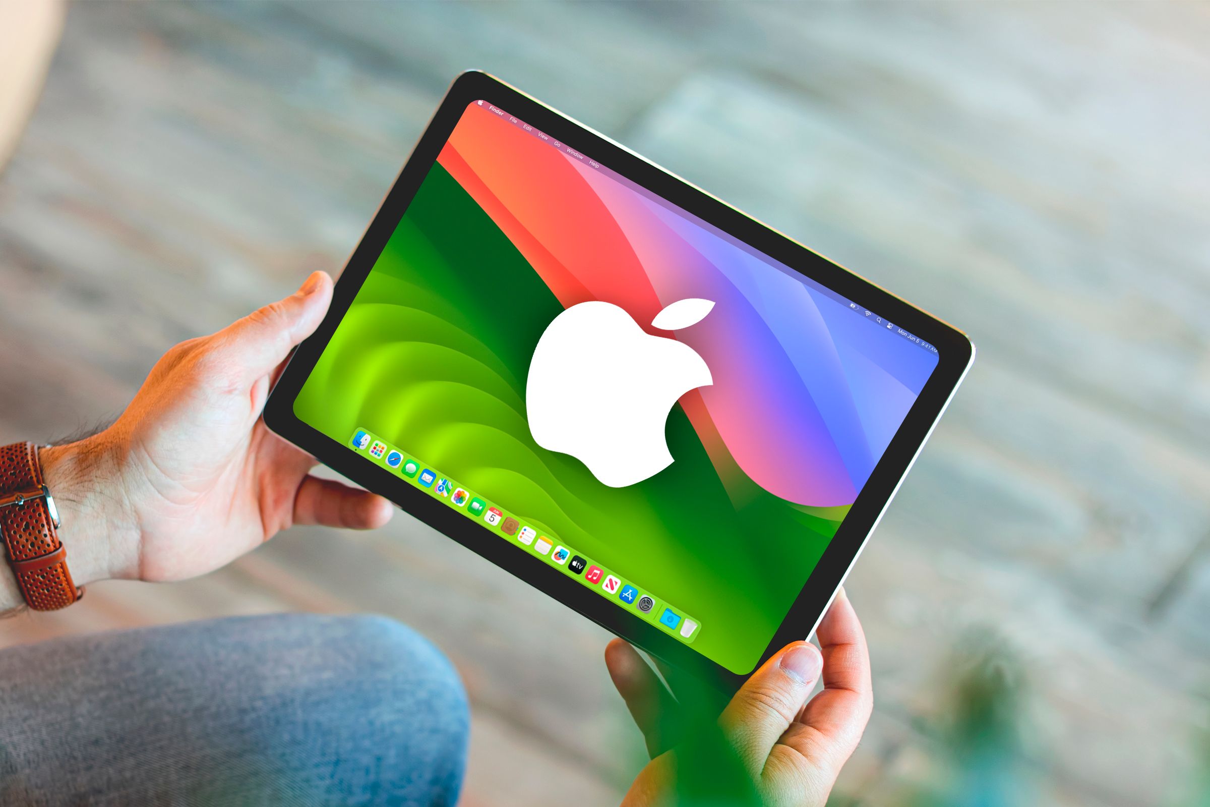A hand holding an iPad running MacOs and the Apple logo on screen