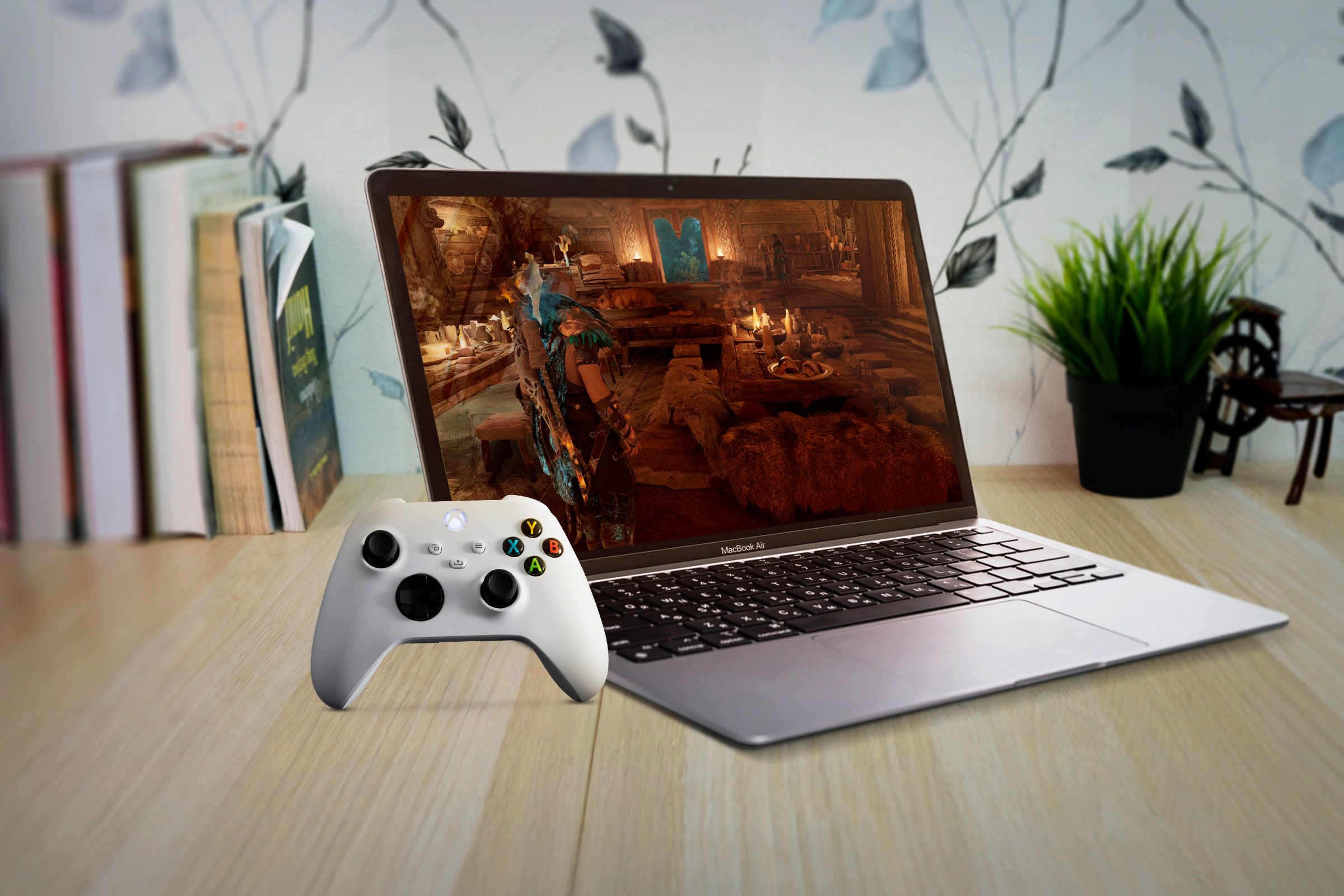 A MacBook Air under a wooden table with a game on the screen and an Xbox controller on the left
