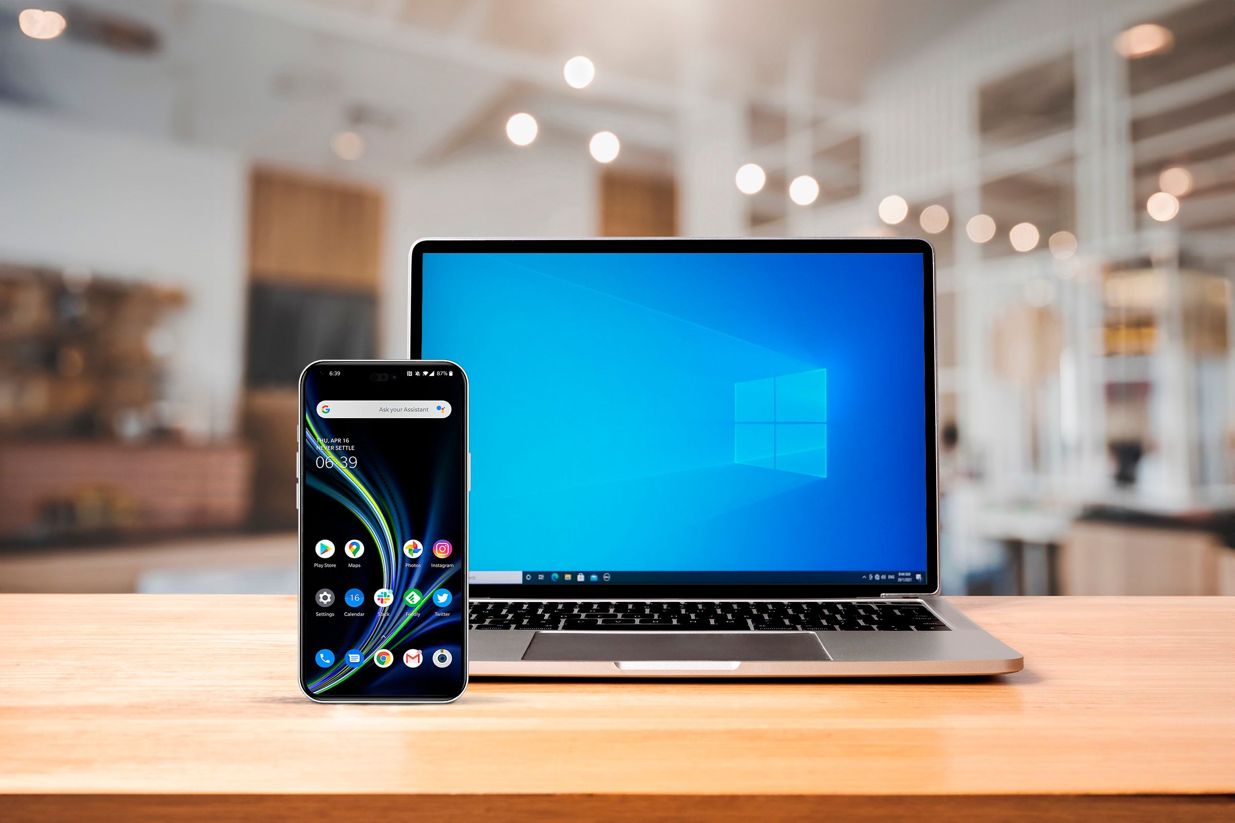 A notebook above a wooden desk with a windows screen and an android smartphone on the front left side-1