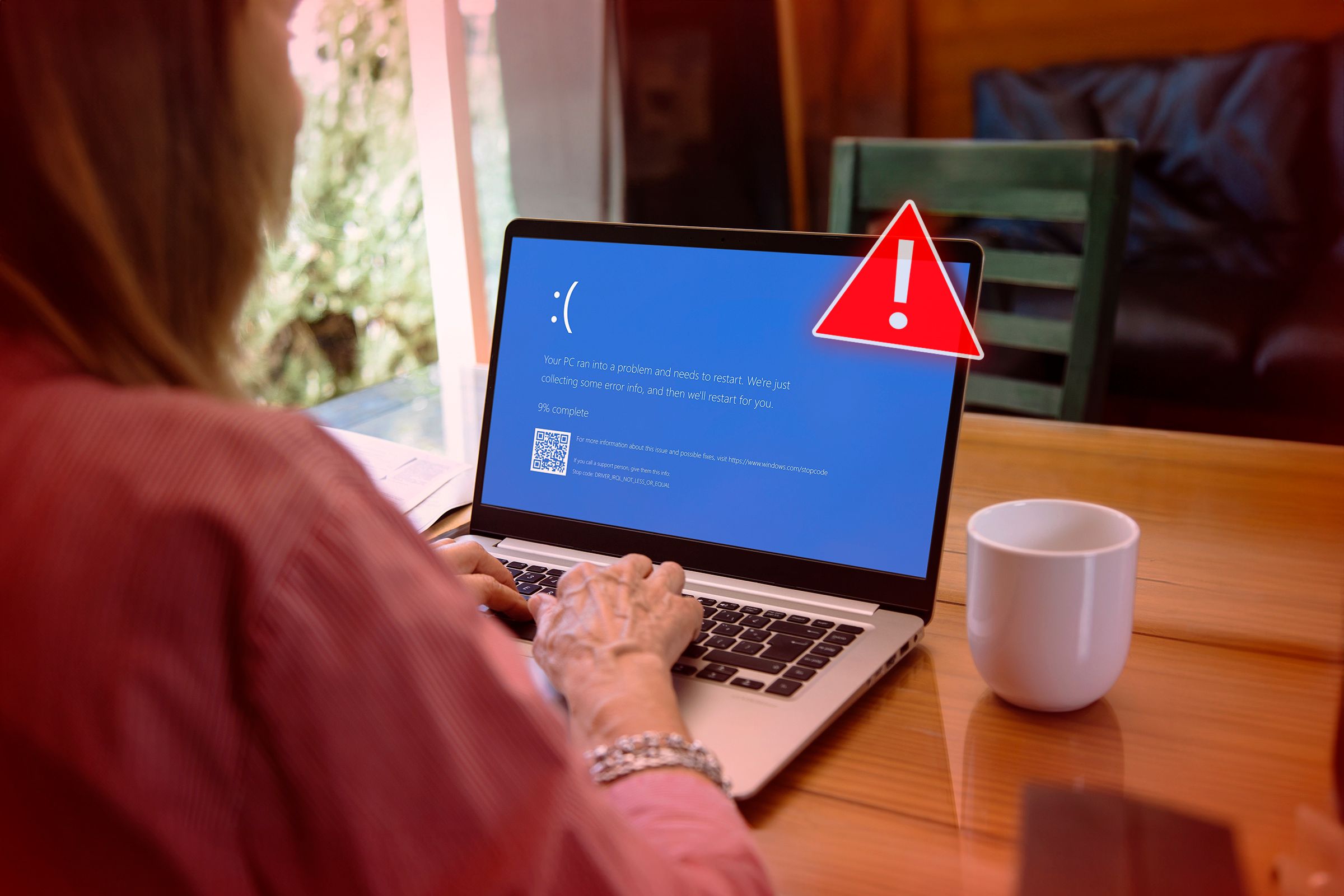 A woman using a laptop with a blue screen that appears when windows randomly shut down and an alert symbol on the front of the laptop