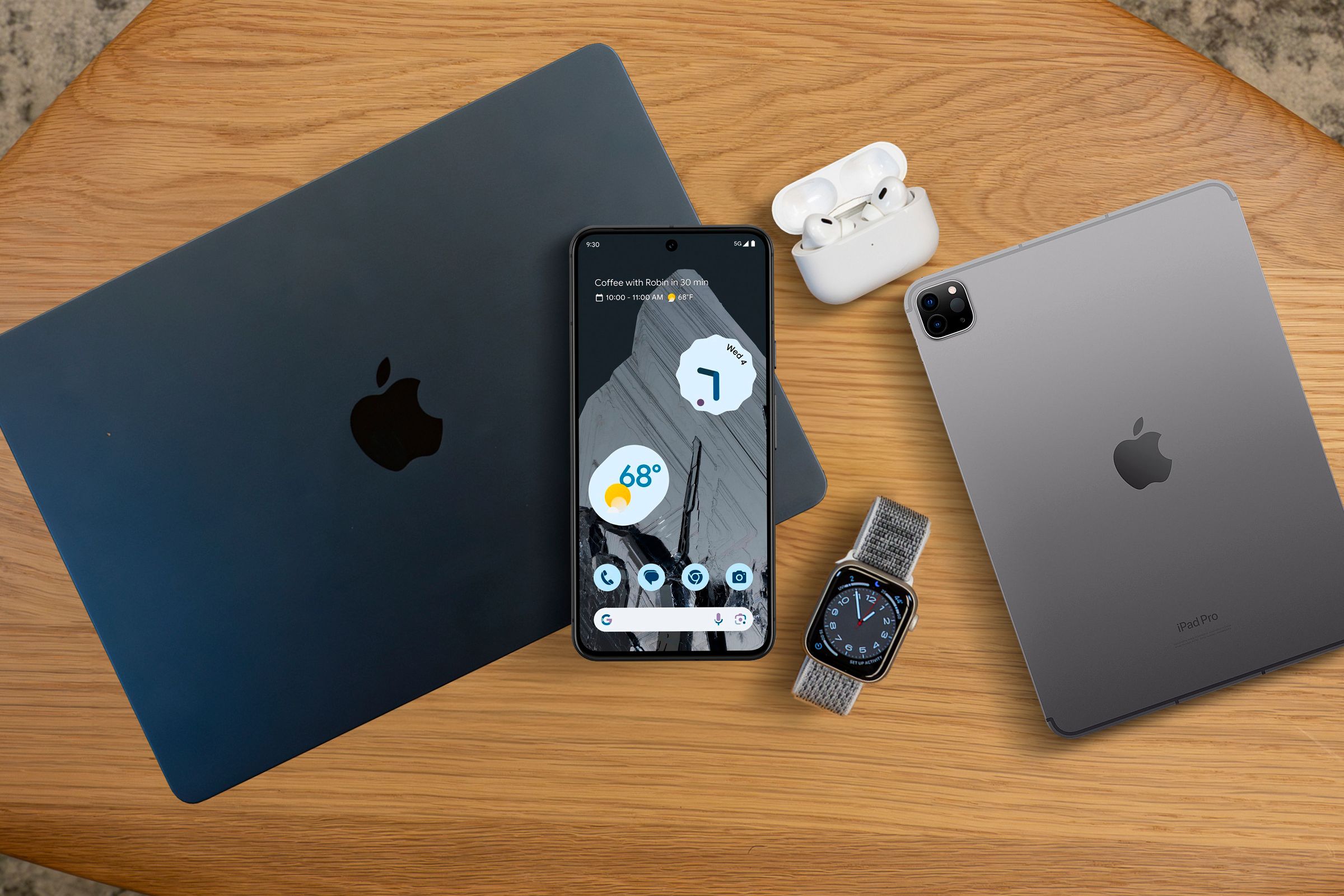 A Macbook, oPad, Airpods, Apple Watch and an Android phone in the center, above the Macbook.