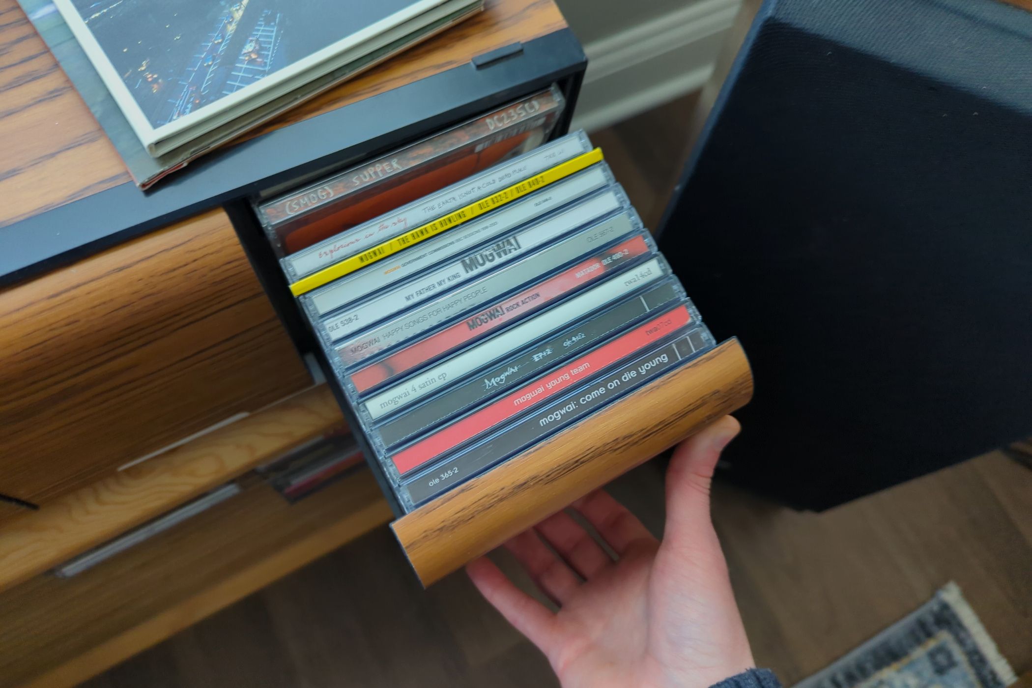 A hand pulls open a drawer full of assorted CD jewel cases.