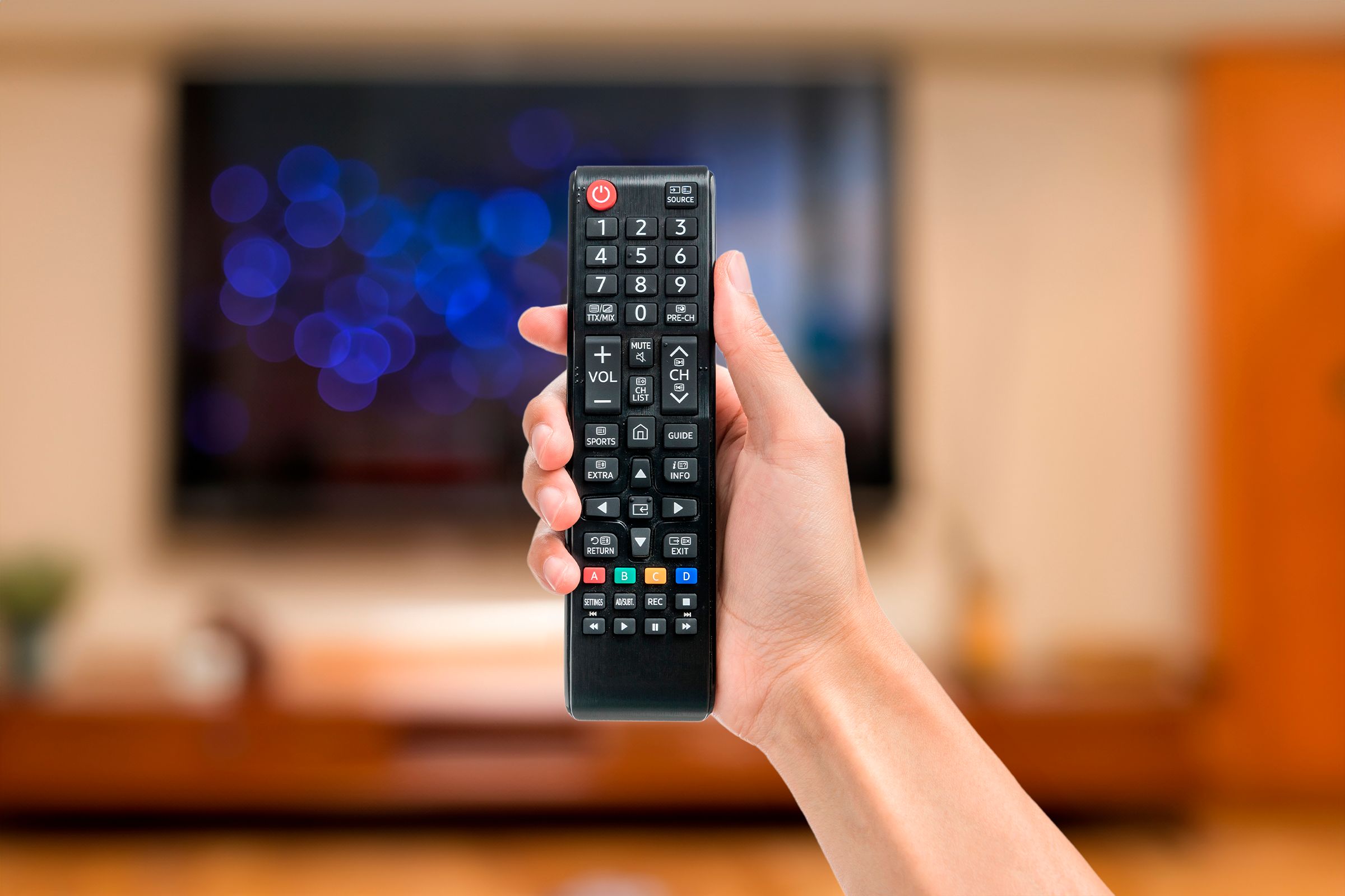 Hand holding an universal TV remote control in a living room.