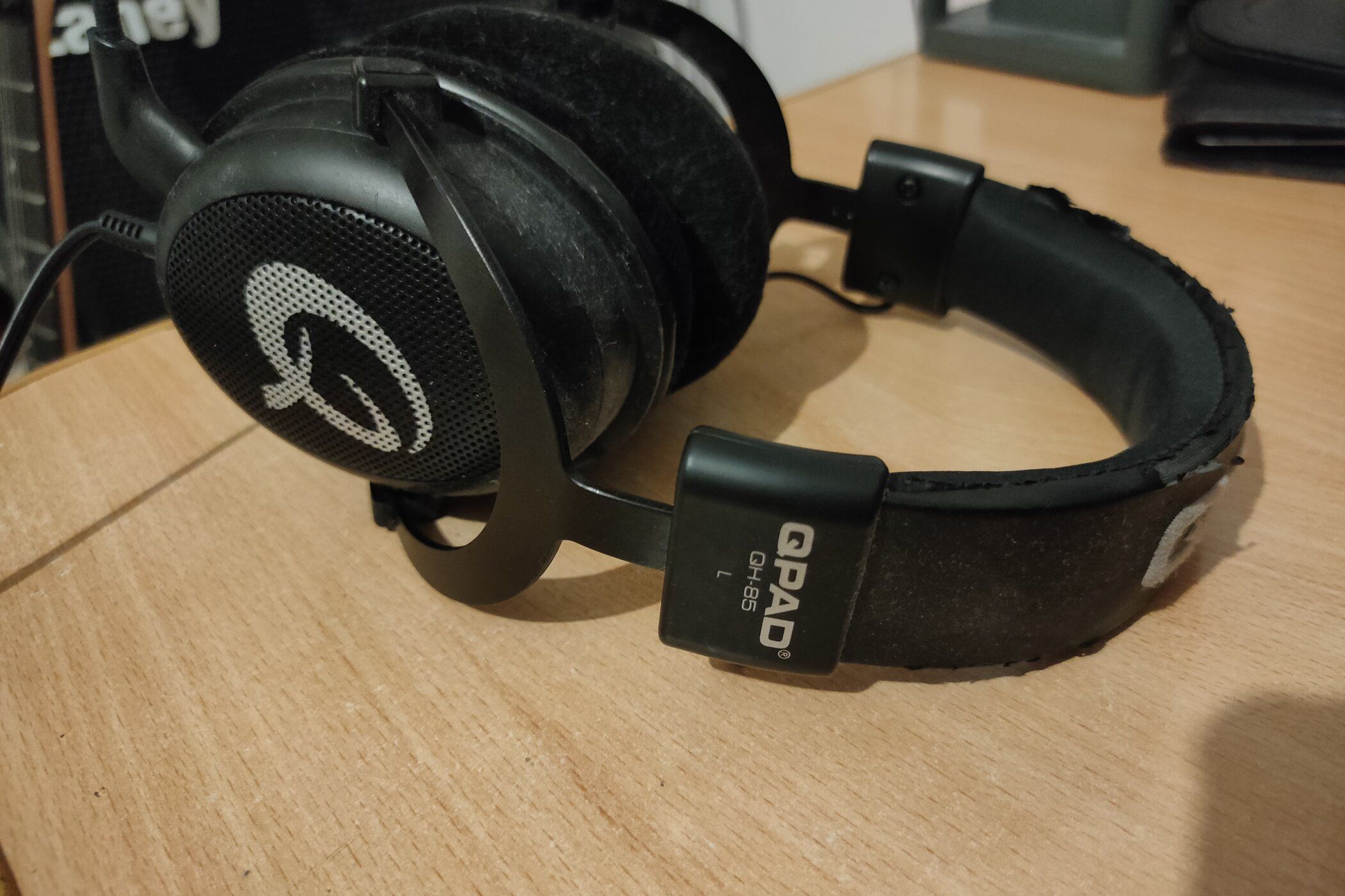 A worn-down pair of QPAD QH-85 gaming headphones on a wooden table.