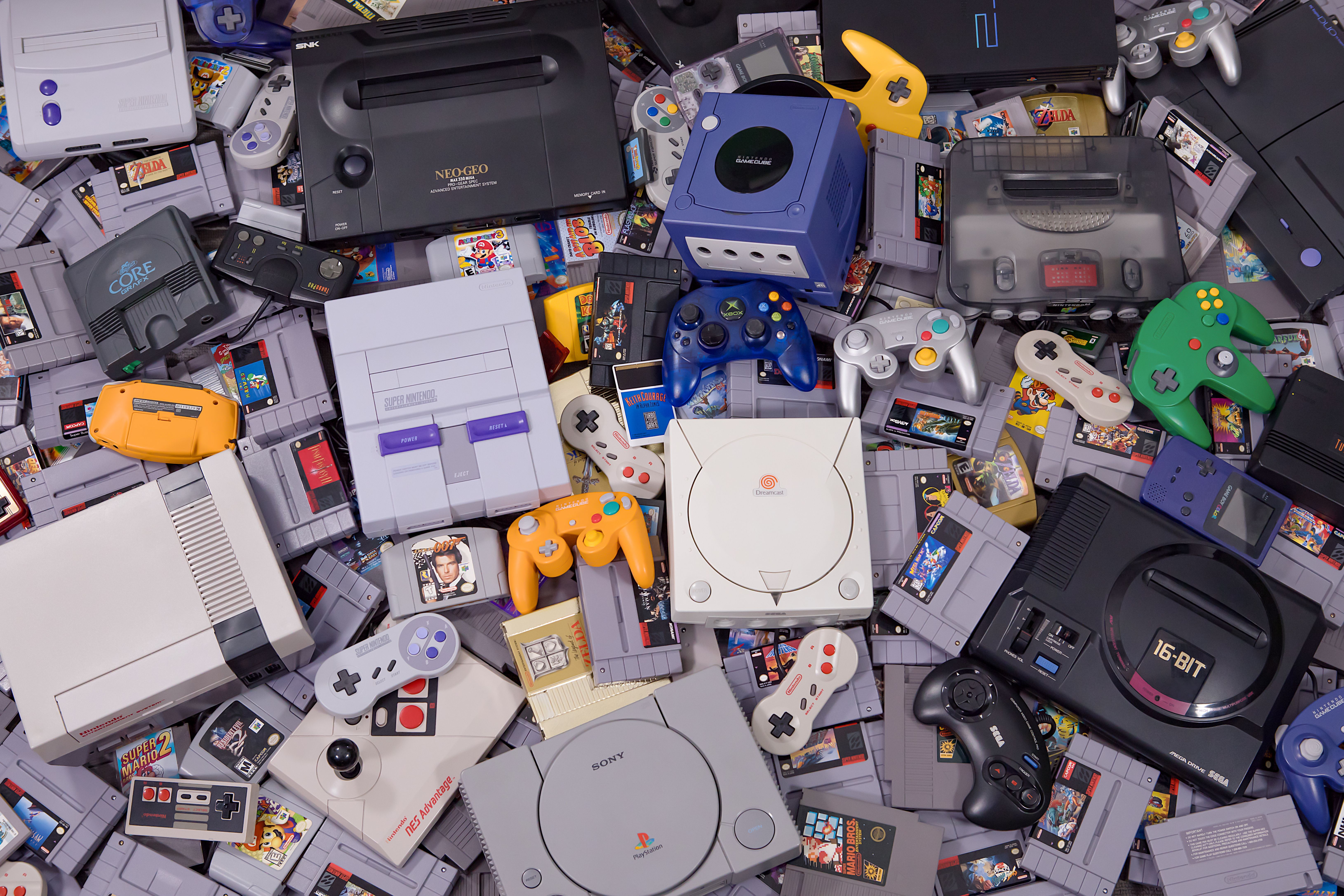 A studio shot of many different old video game systems, controllers and game cartridges shot from above.