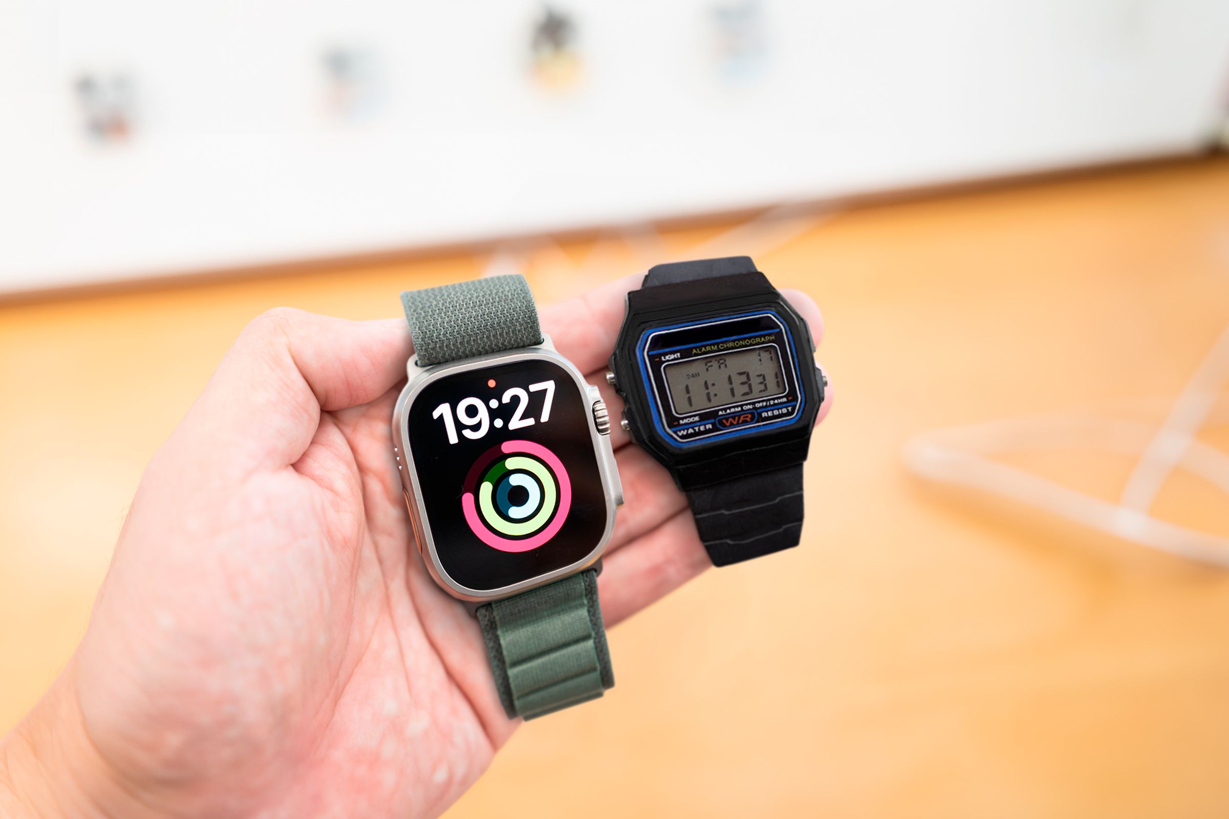 A hand holding an Apple Watch Ultra on the left side, and a Casio F-91W on the right side