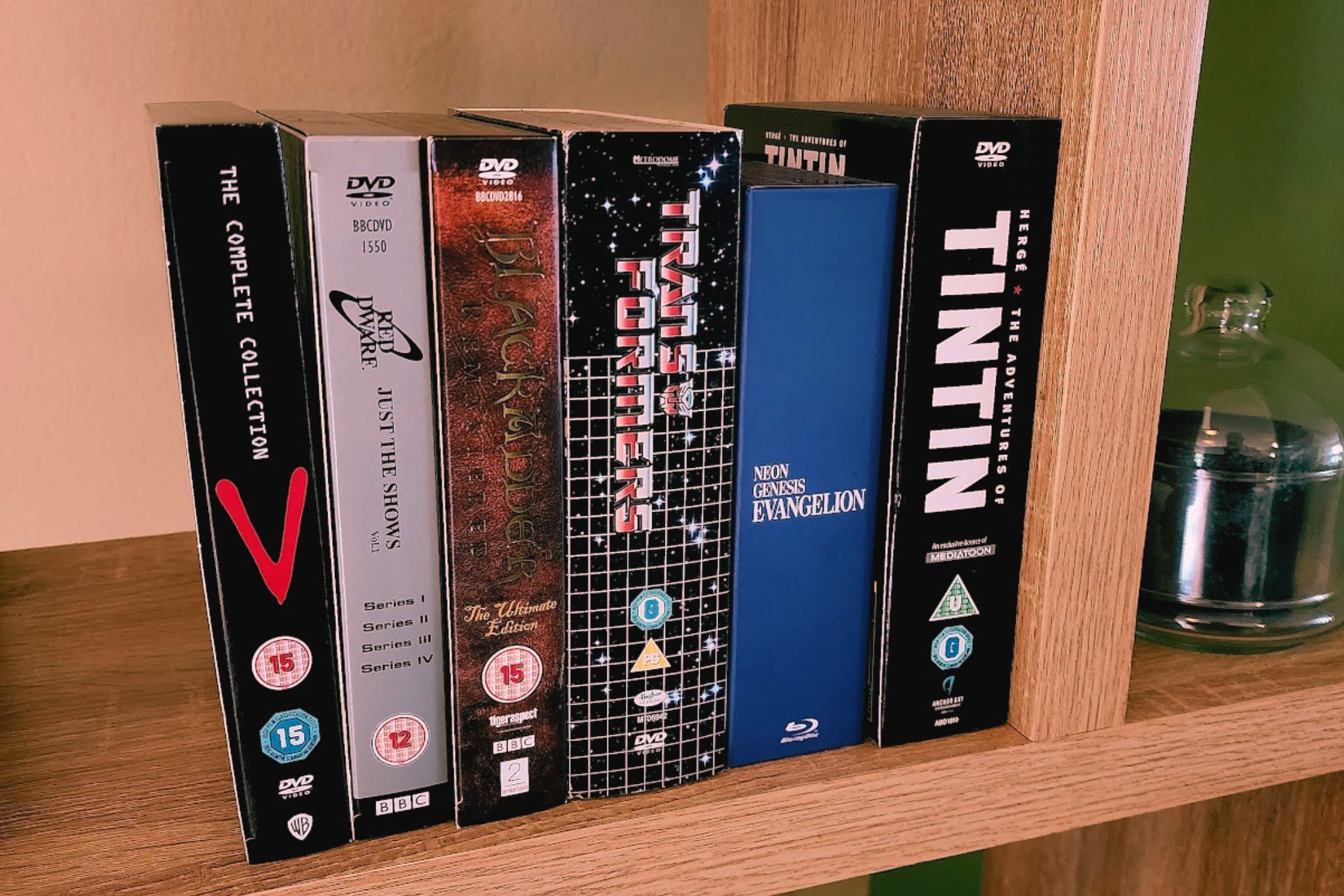 A shelf with several TV series box sets on it, including Red Dwarf, Transformers, Tintin, Black Adder, V the Series, and Neon Genesis Evangelion