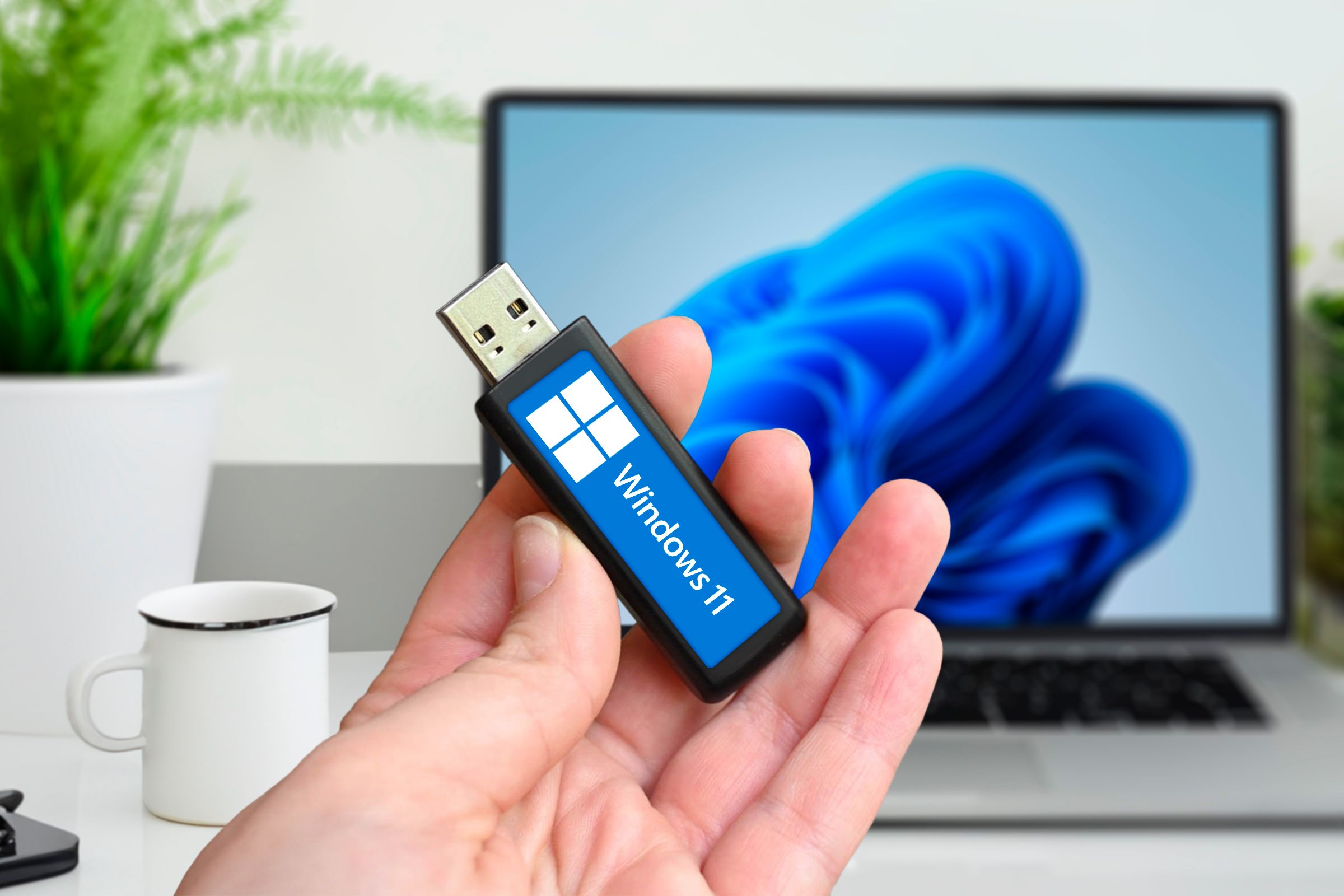 Person holding a USB drive with Windows 11 and a laptop in the background.